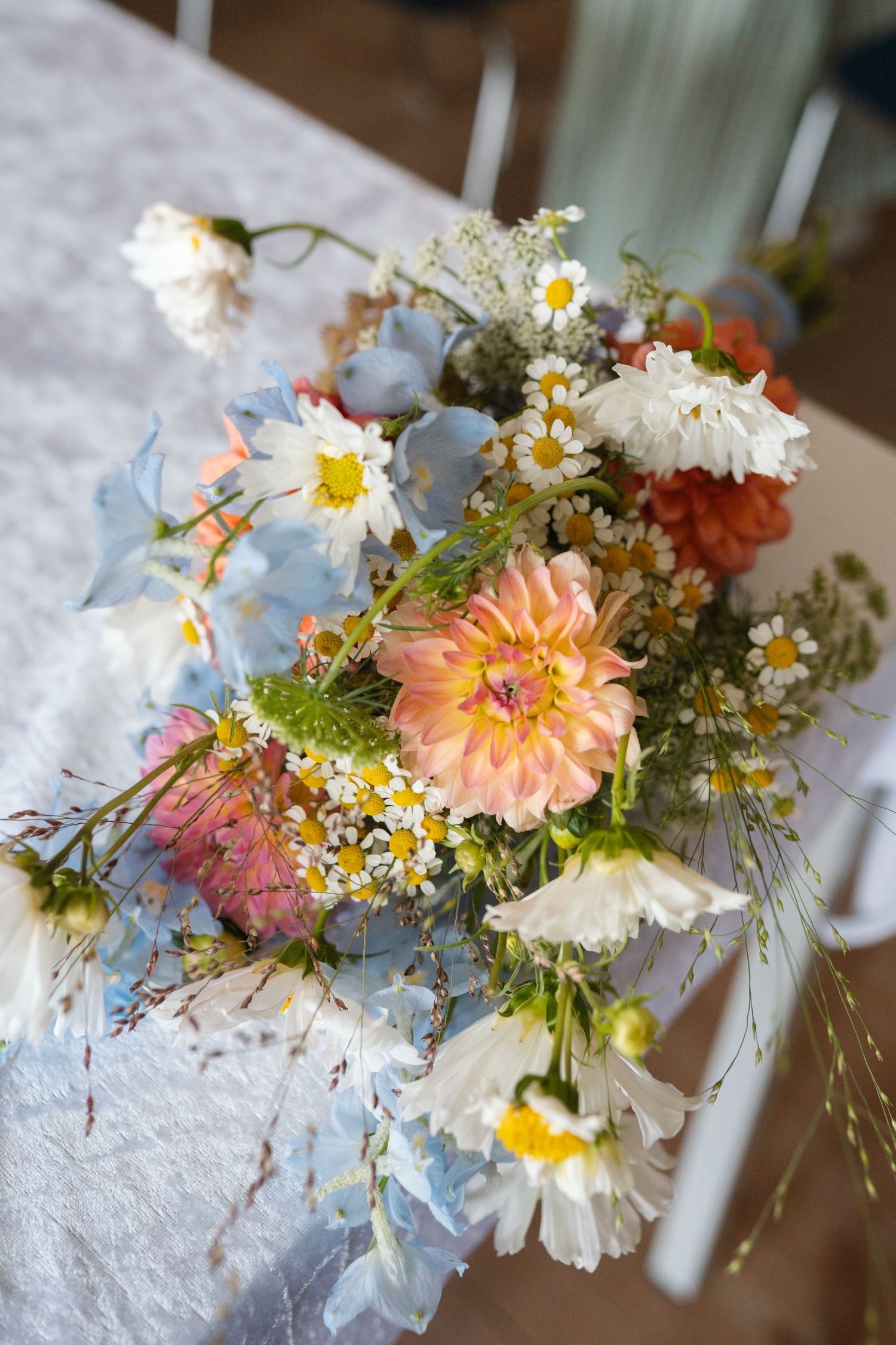 Colorful wildflower bouquet with dahlias, daisies, and chamomile on a white lace tablecloth.