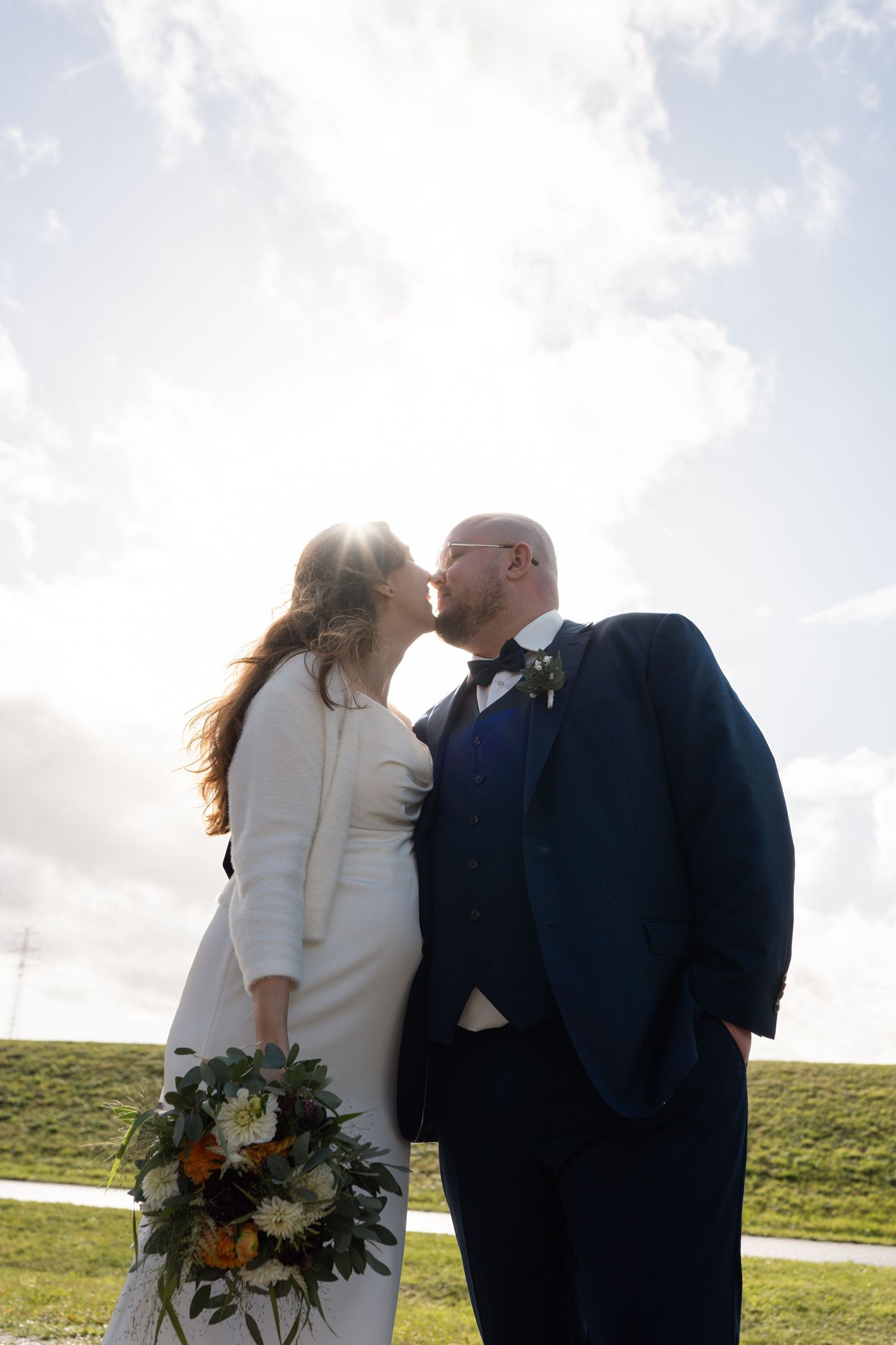 Couple shares an intimate moment outdoors with scenic rolling hills and cloudy sky in the background.