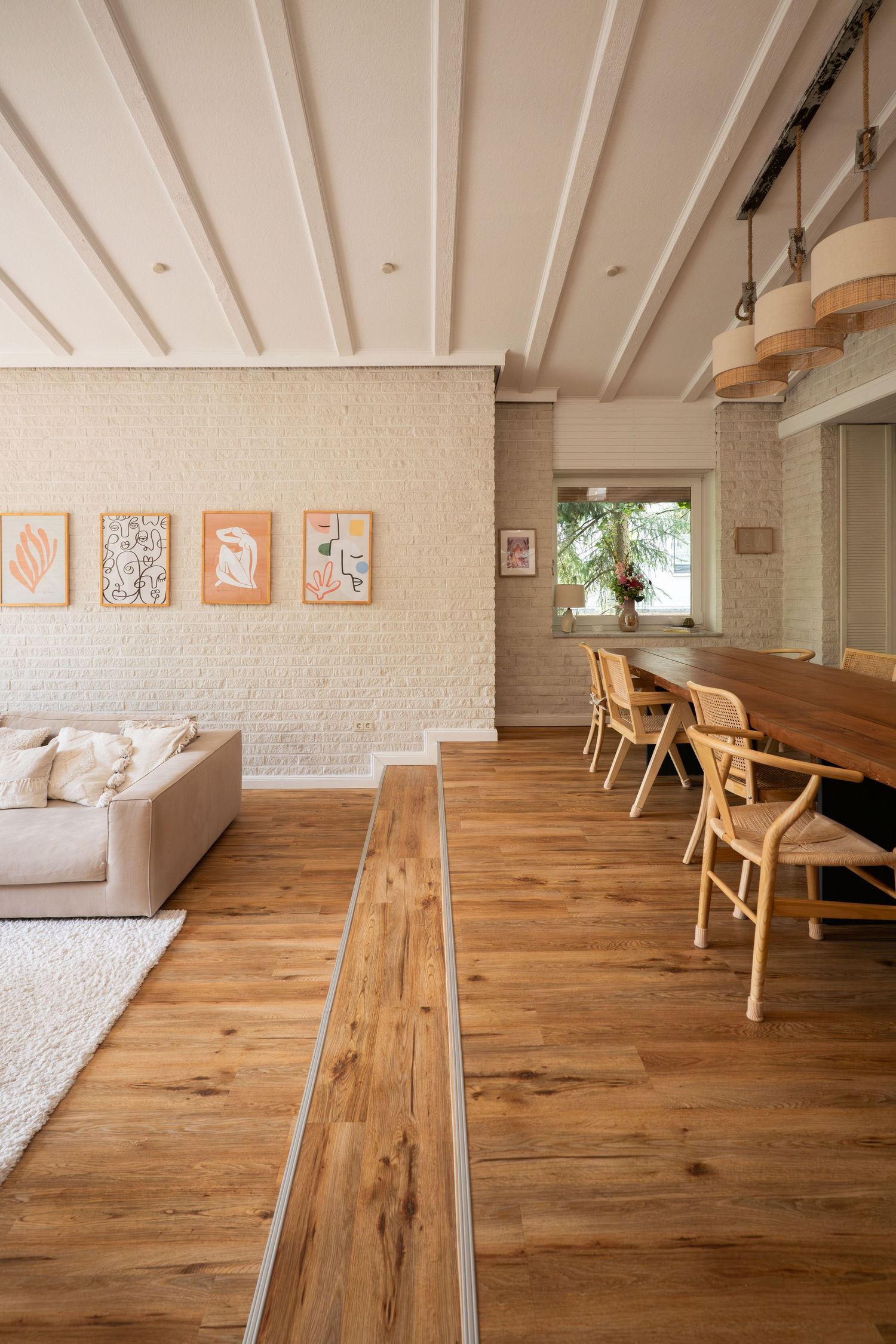 Rustic wood flooring extends across a bright attic space with white walls and wooden beams.