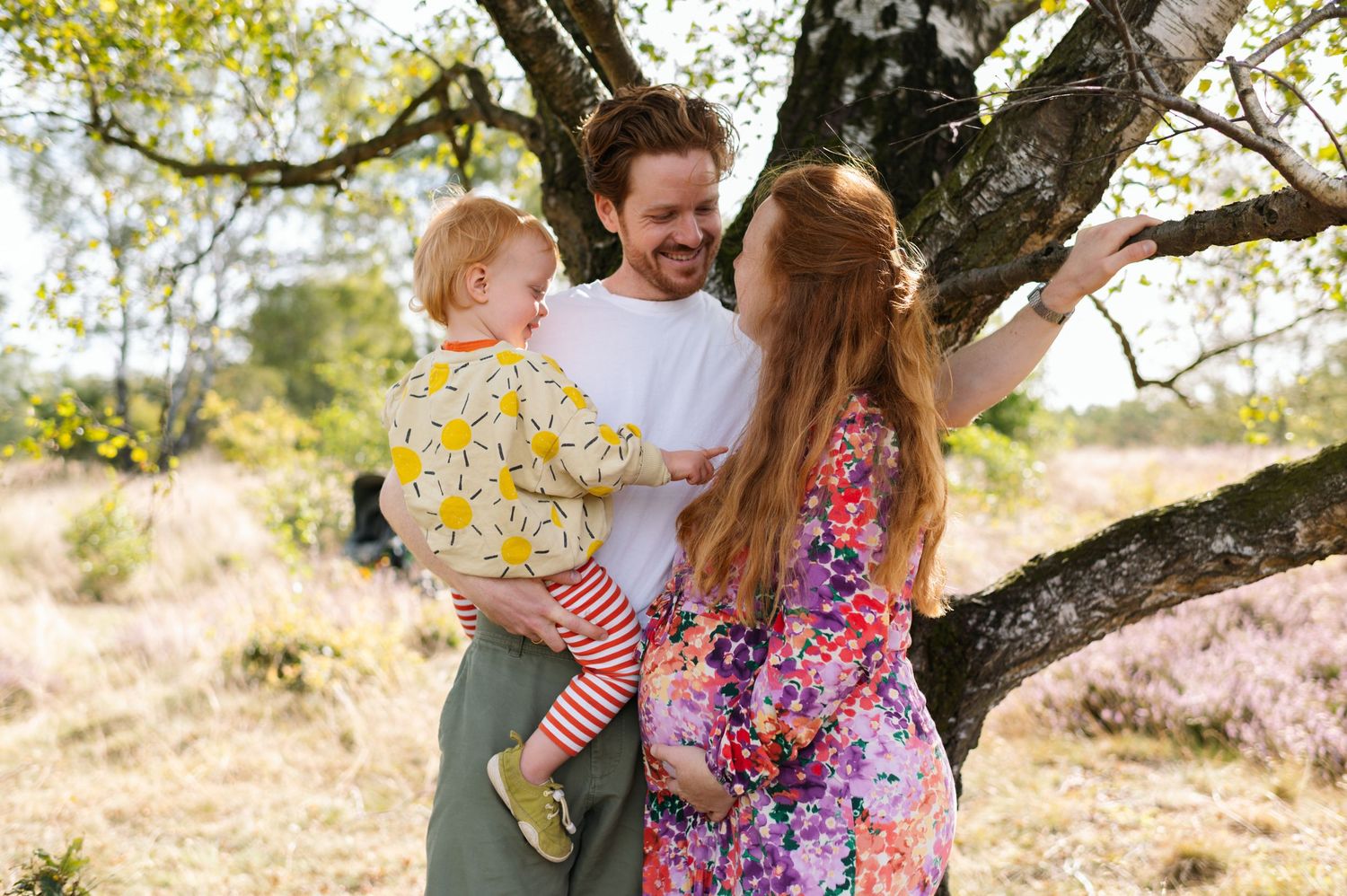 Family members embrace and laugh together during a sunny outdoor photo session in a blooming spring landscape.