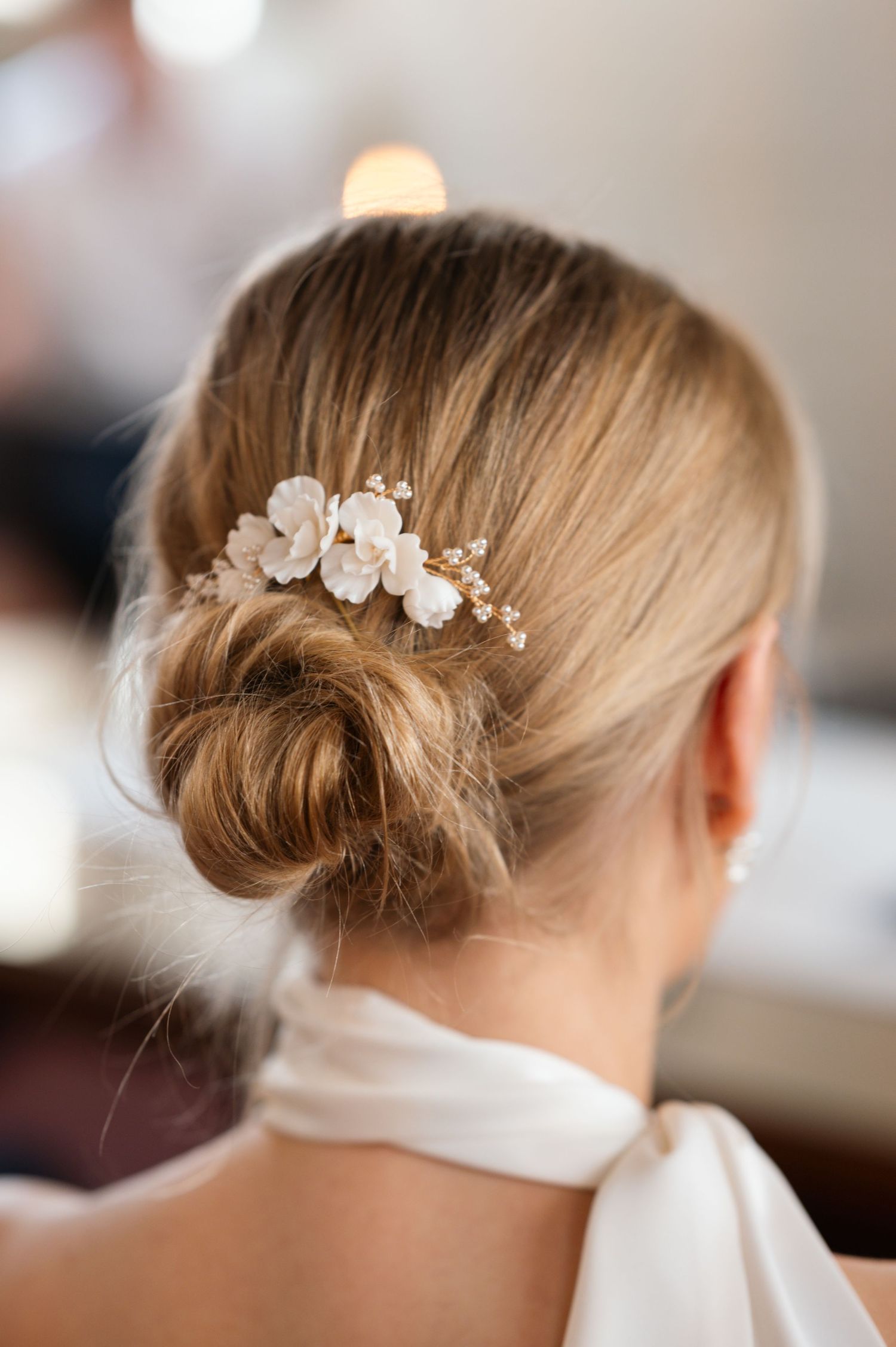 Elegant bridal low bun hairstyle adorned with delicate white floral hair comb and gold accents.