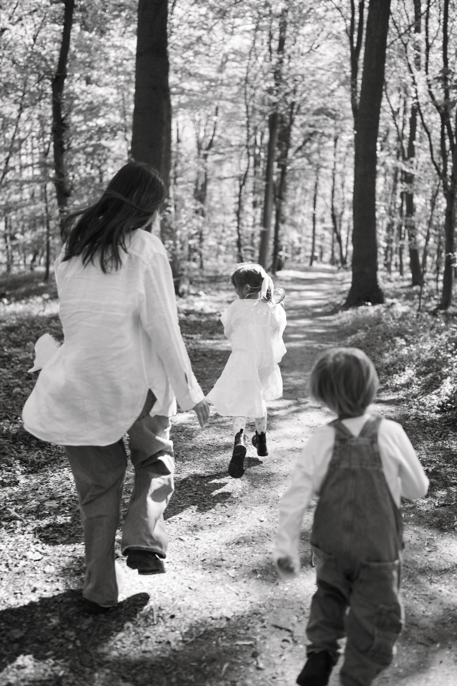 Black and white photo of a mother walking with two young children on a forest path.
