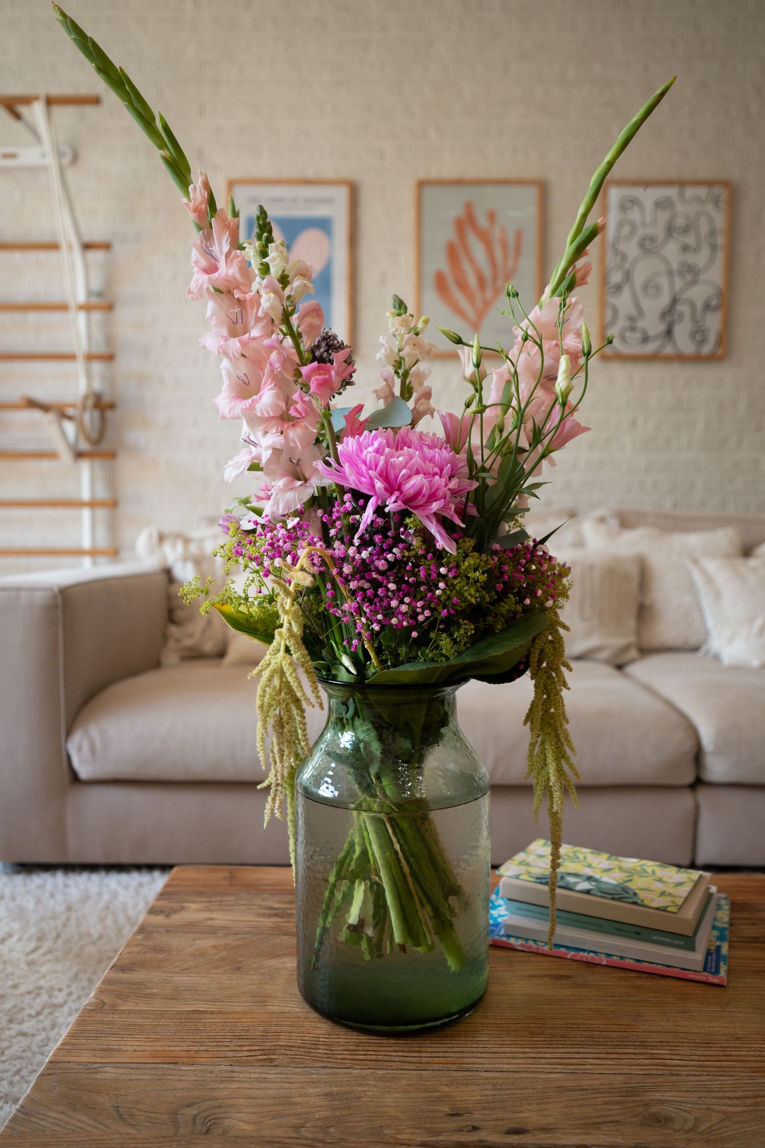Pink and purple flowers arranged in a glass jar on a rustic wooden table with living room decor in the background.