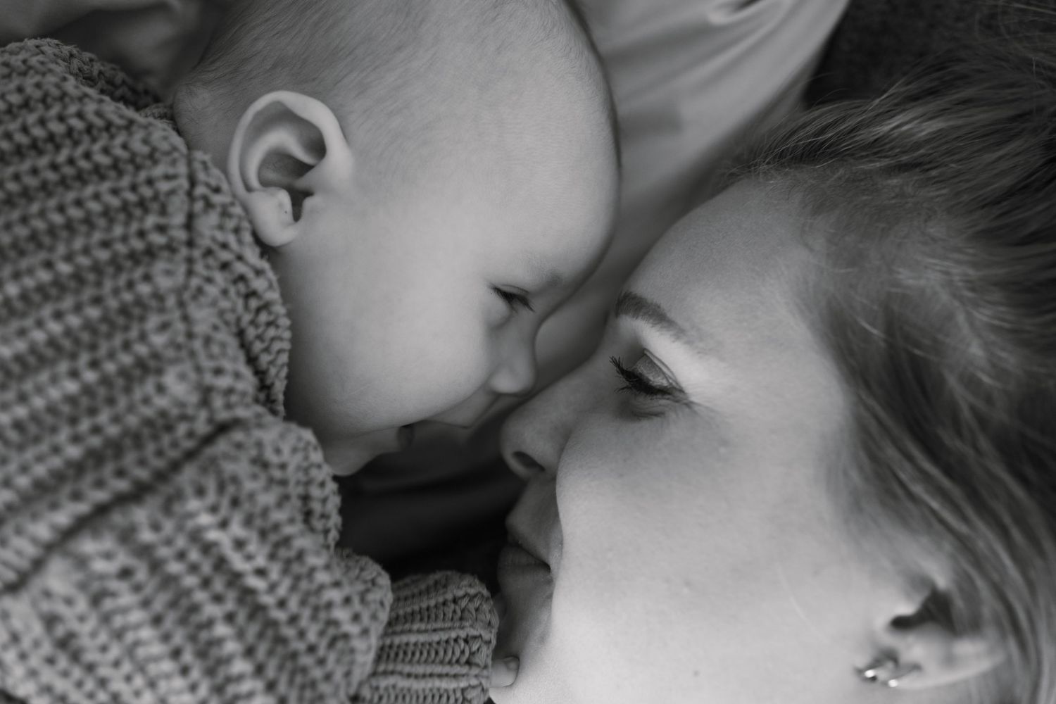 Black and white photo of a mother and baby touching noses tenderly in an intimate bonding moment.