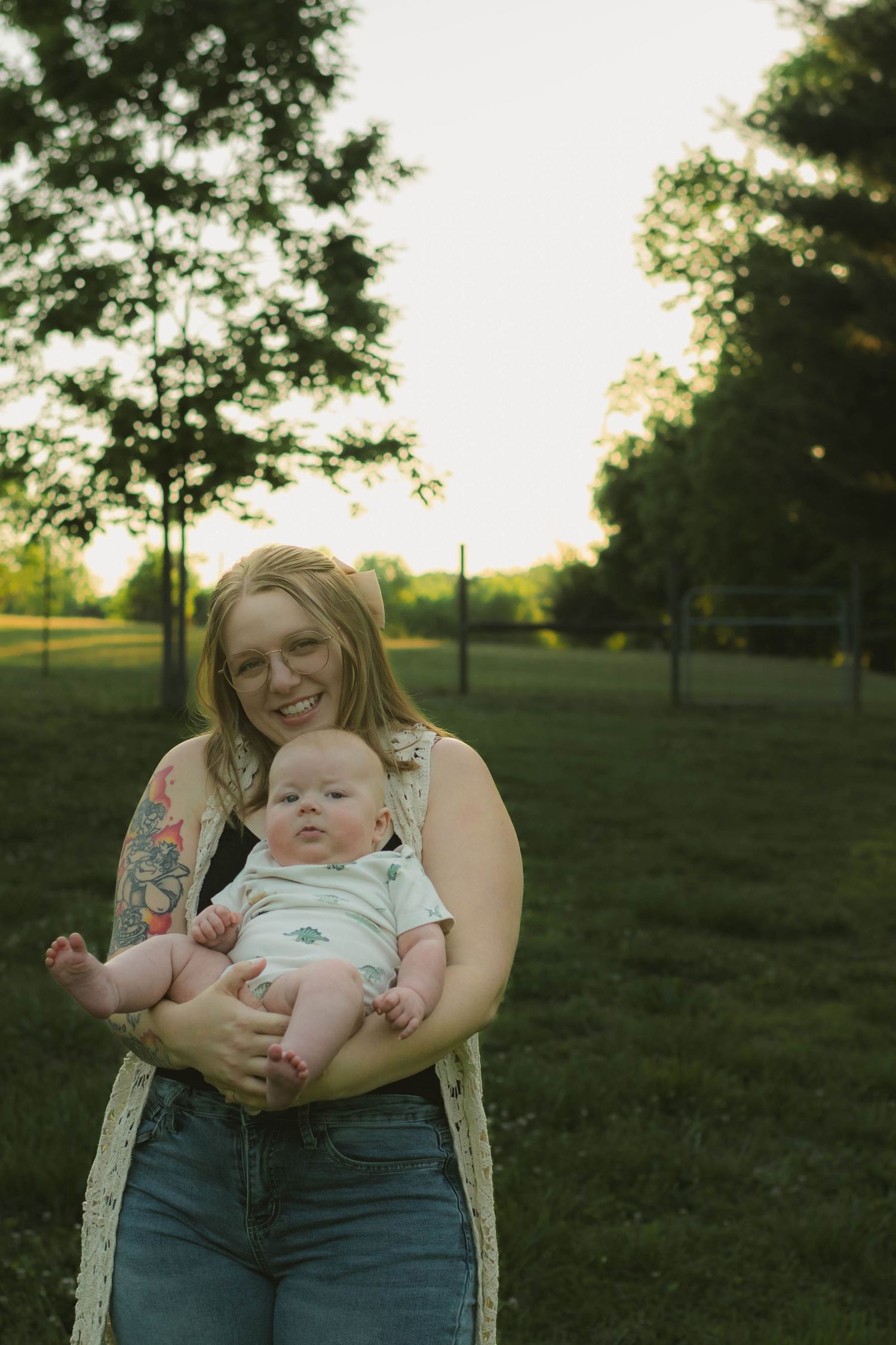 Smiling mother holding her baby in a sunny green park at golden hour.