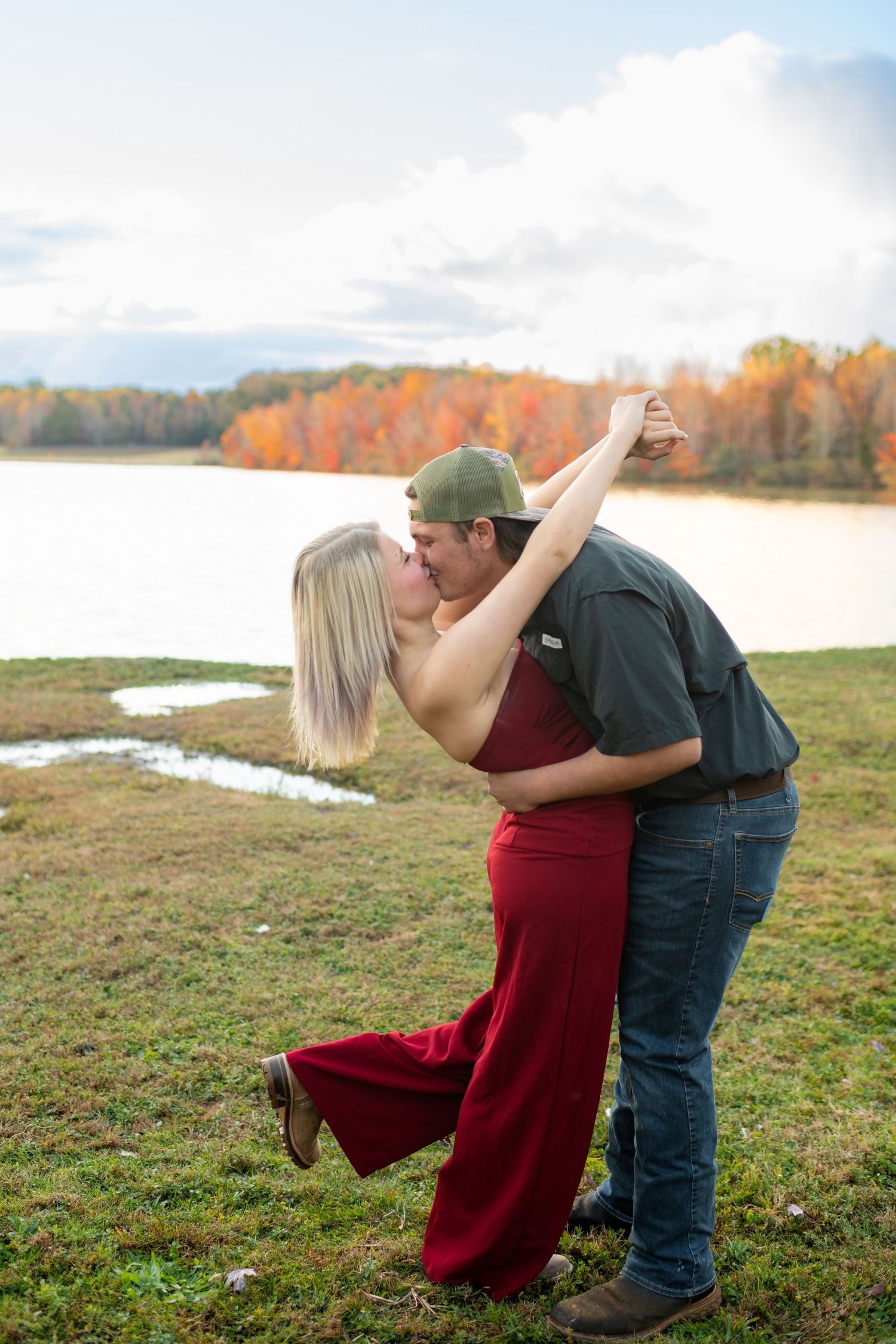 Couple sharing a romantic dip kiss by a scenic lake with brilliant fall foliage in the background.