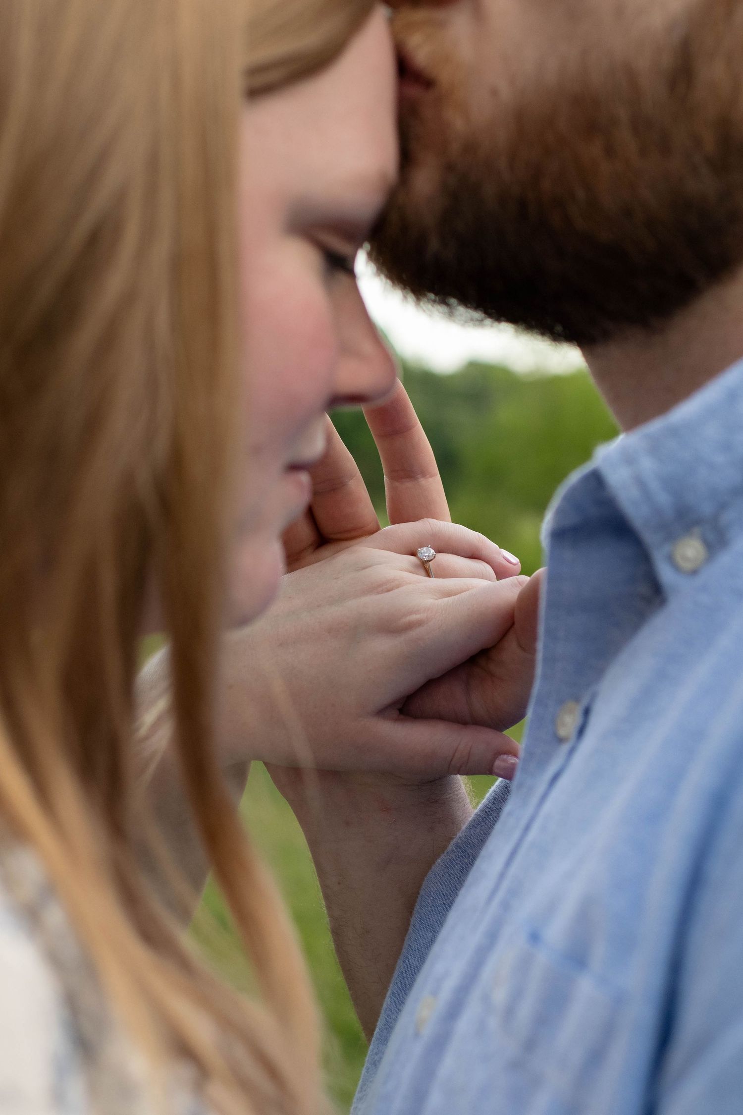 Intimate close-up of bearded man kissing womans forehead while she displays her diamond engagement ring.