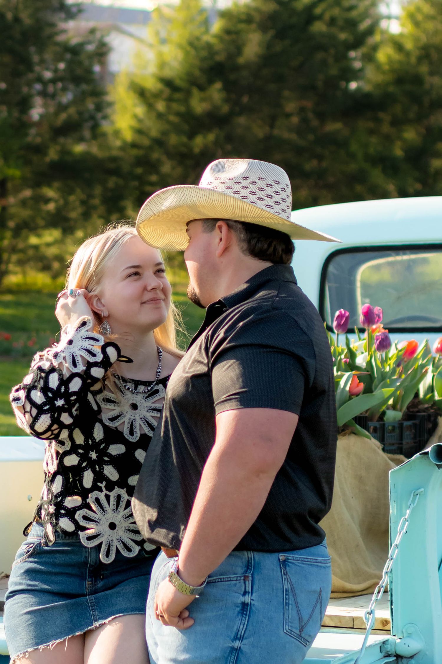 Couple gazing at each other near a vintage teal truck with tulips, man in straw cowboy hat.