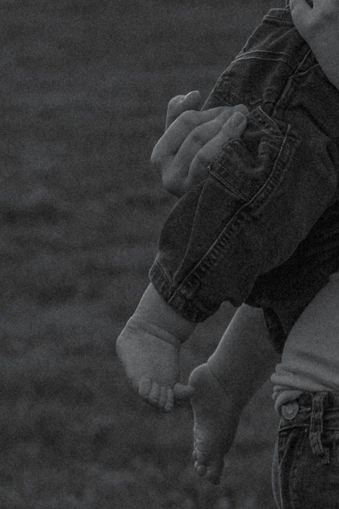 Black and white photo of an adult holding a baby by the legs outdoors.