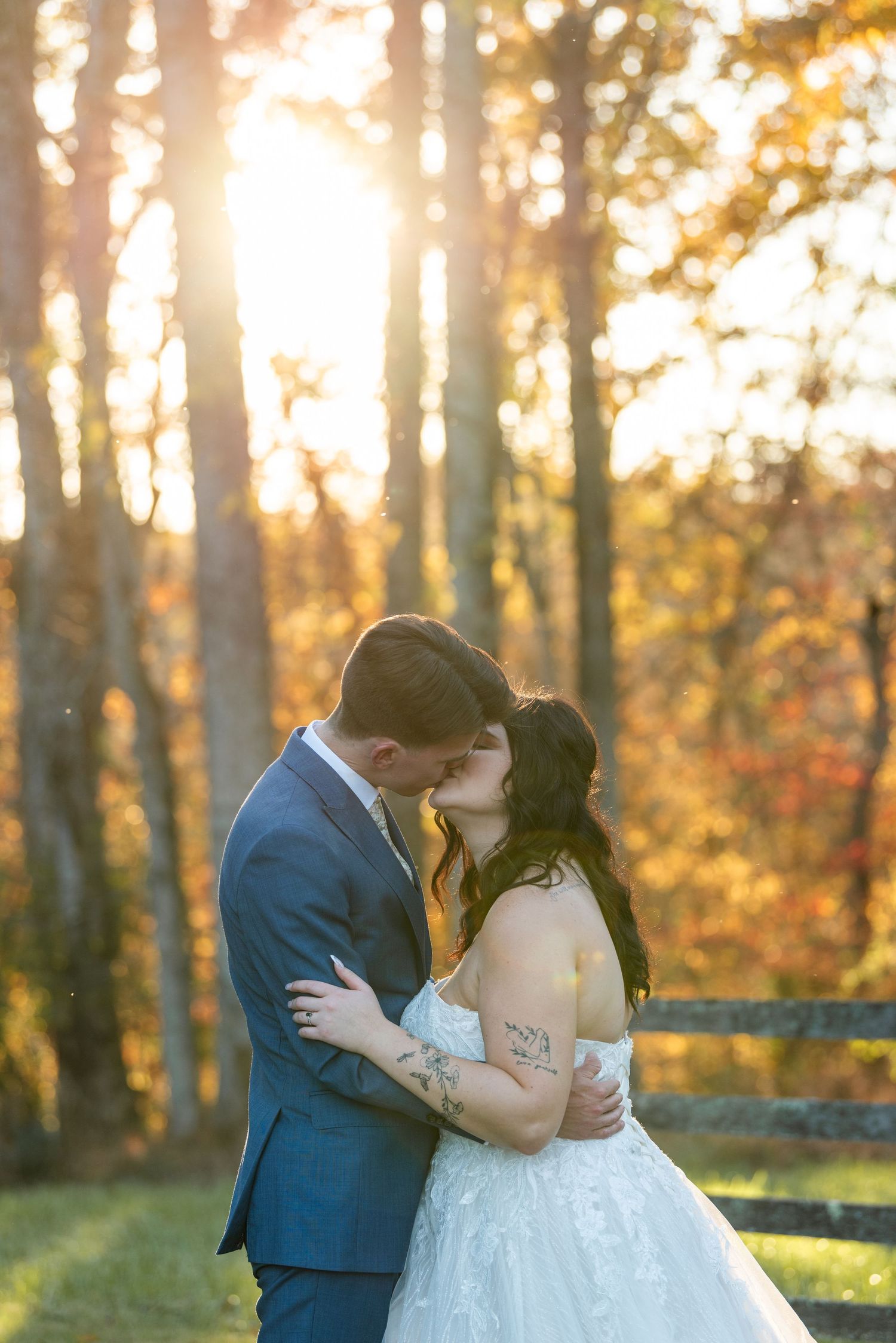 Bride and groom sharing a kiss in golden sunlight among autumn foliage at wedding.
