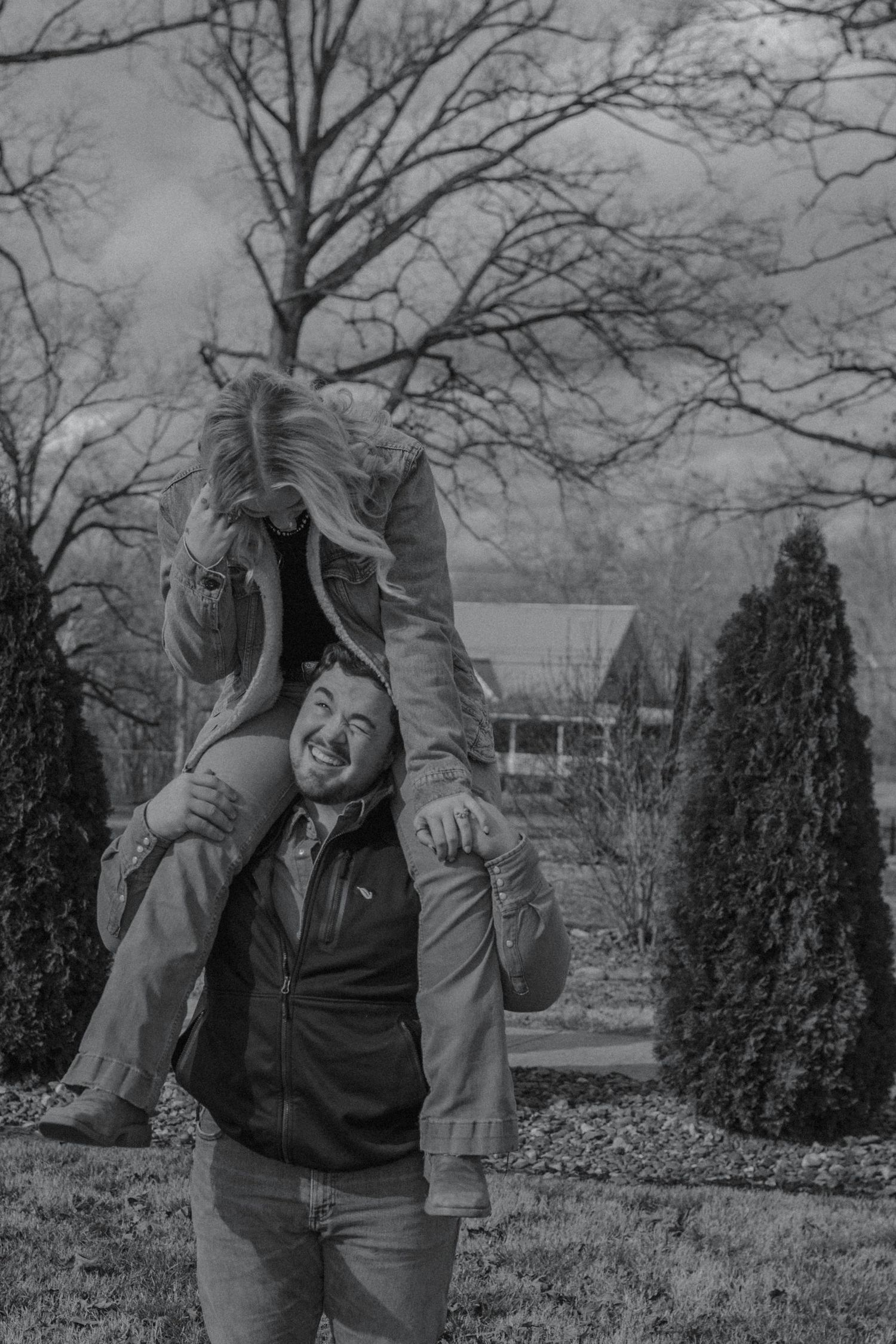 Black and white photo of a joyful man carrying his girlfriend on his shoulders outdoors in winter.