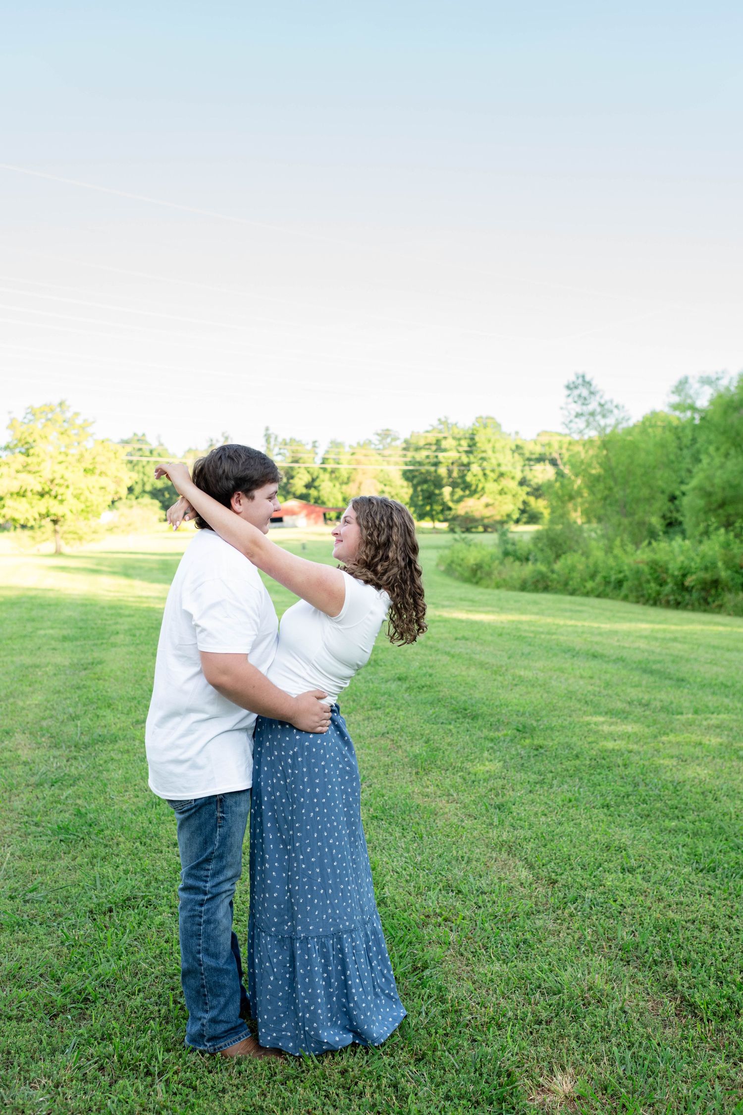 Young couple dancing together in open green field during golden hour engagement session.