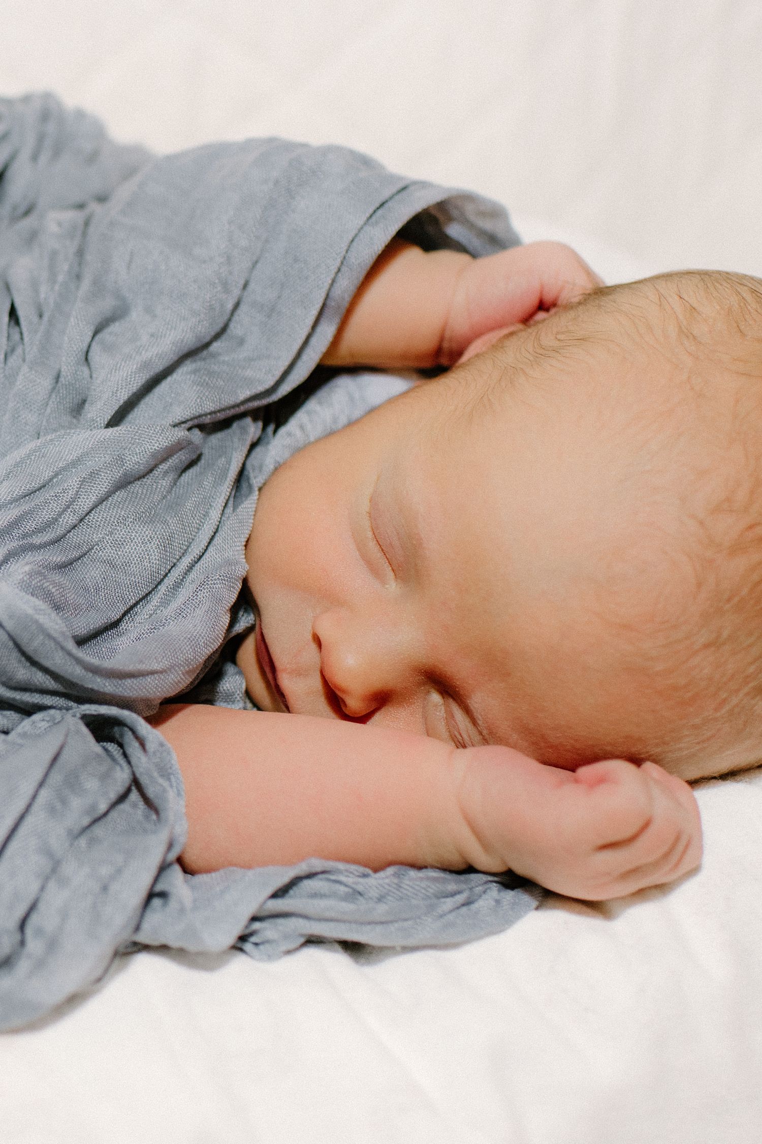 Newborn baby sleeping peacefully wrapped in a soft blue muslin swaddle blanket.