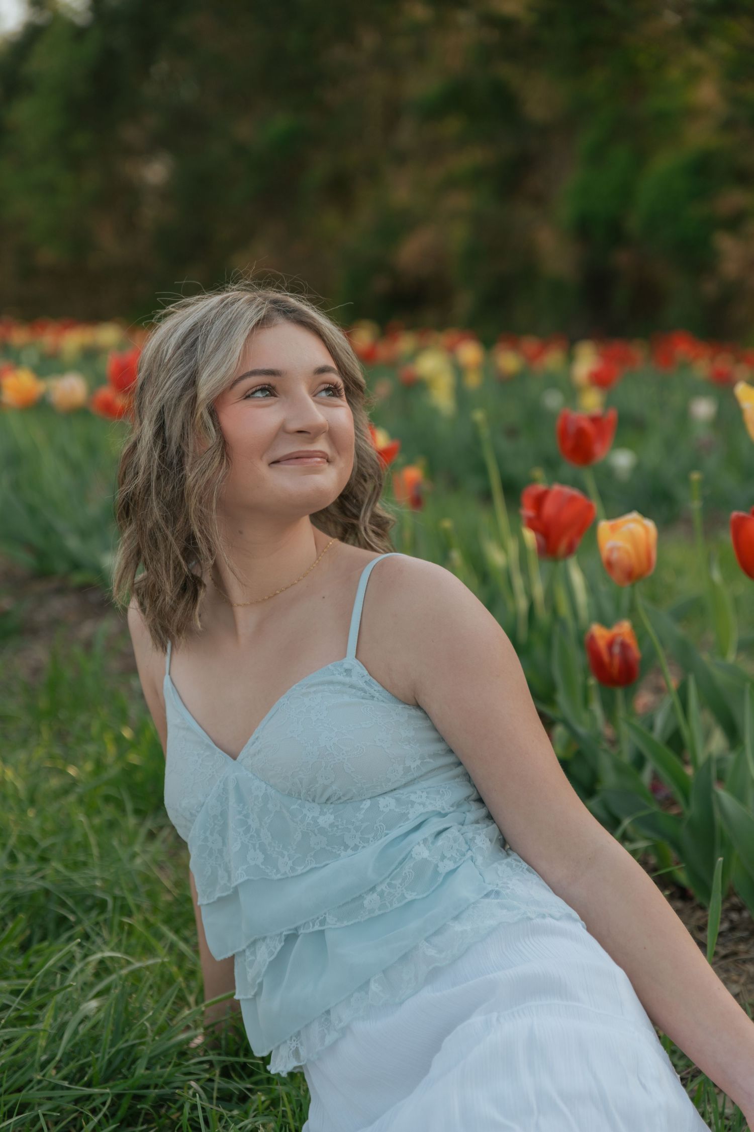 Young woman in light blue dress sitting in a vibrant tulip field smiling at sunset.