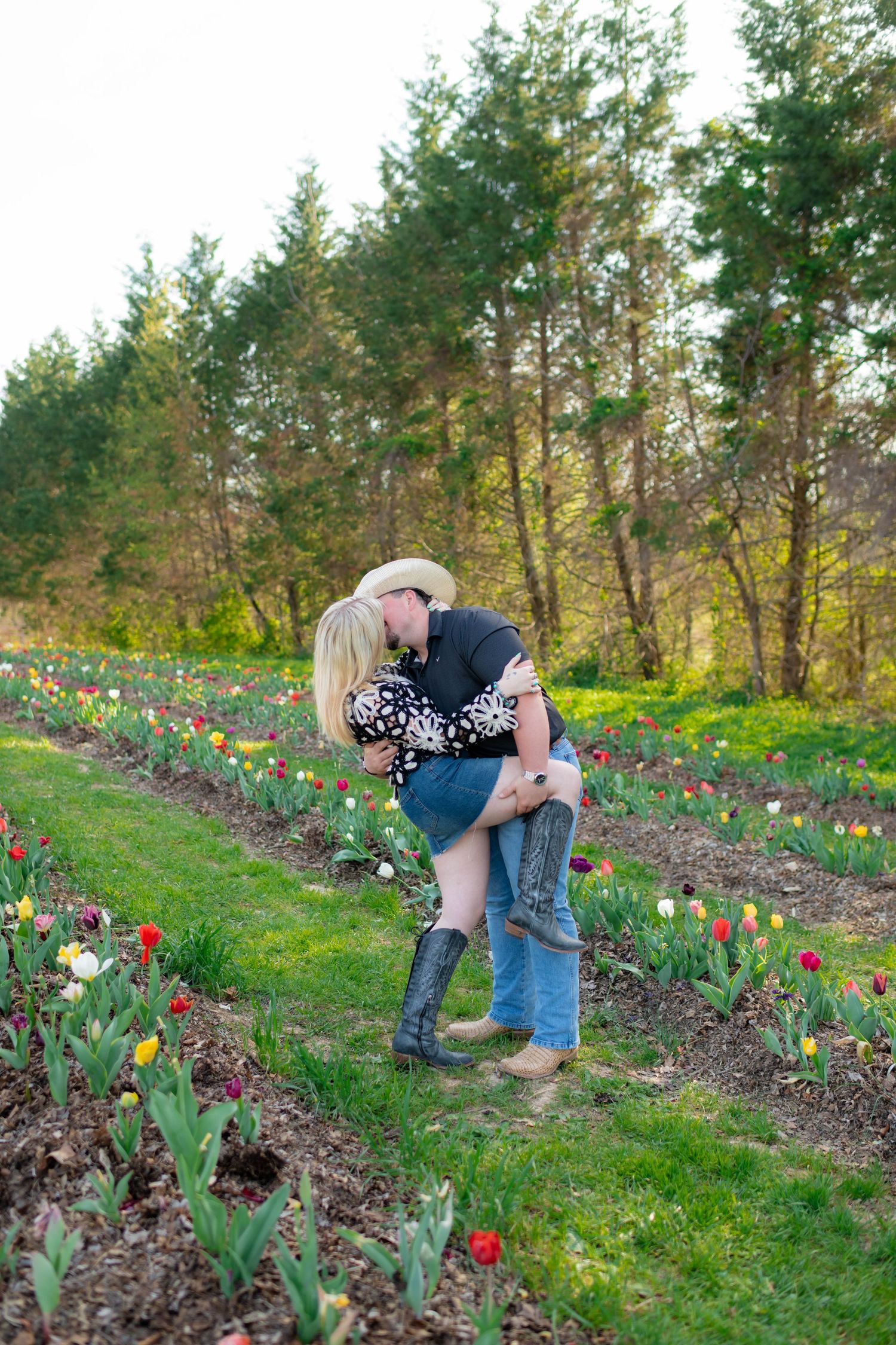 Couple sharing romantic kiss among colorful tulip rows in lush green garden setting.