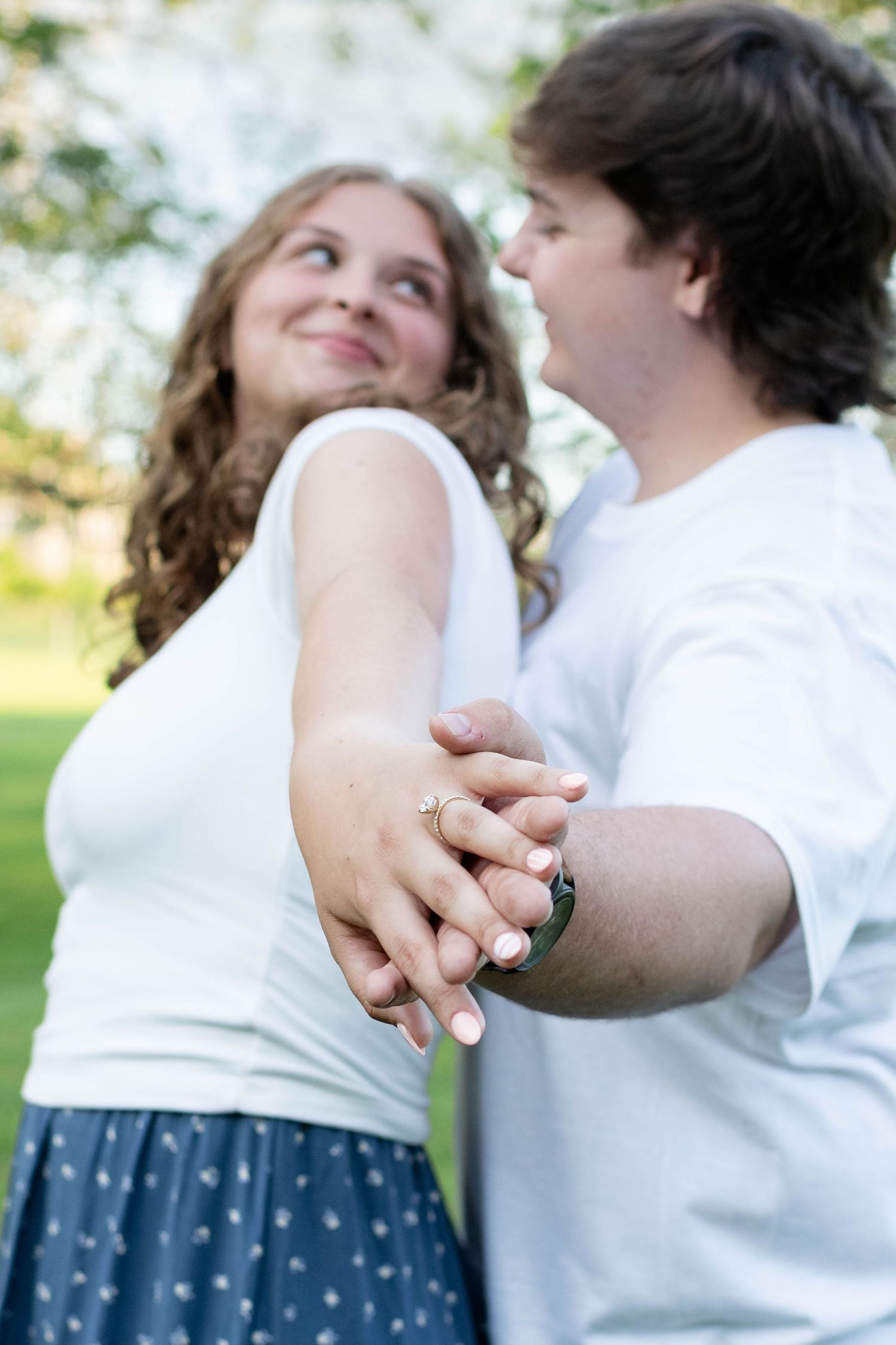 Couple holding hands and gazing at each other with engagement ring visible in foreground.