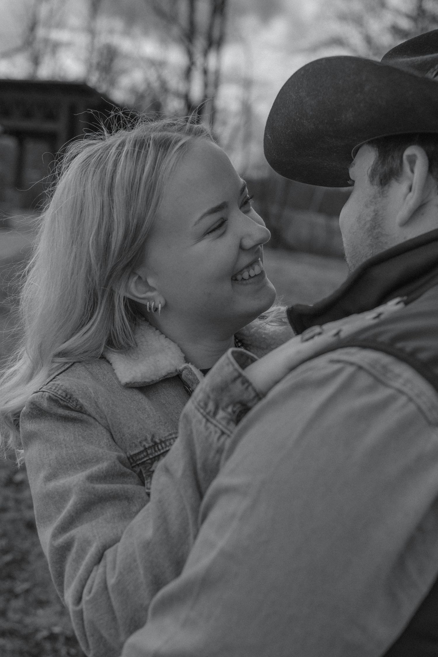 Black and white photo of smiling couple gazing at each other, woman in denim jacket and man in cowboy hat.