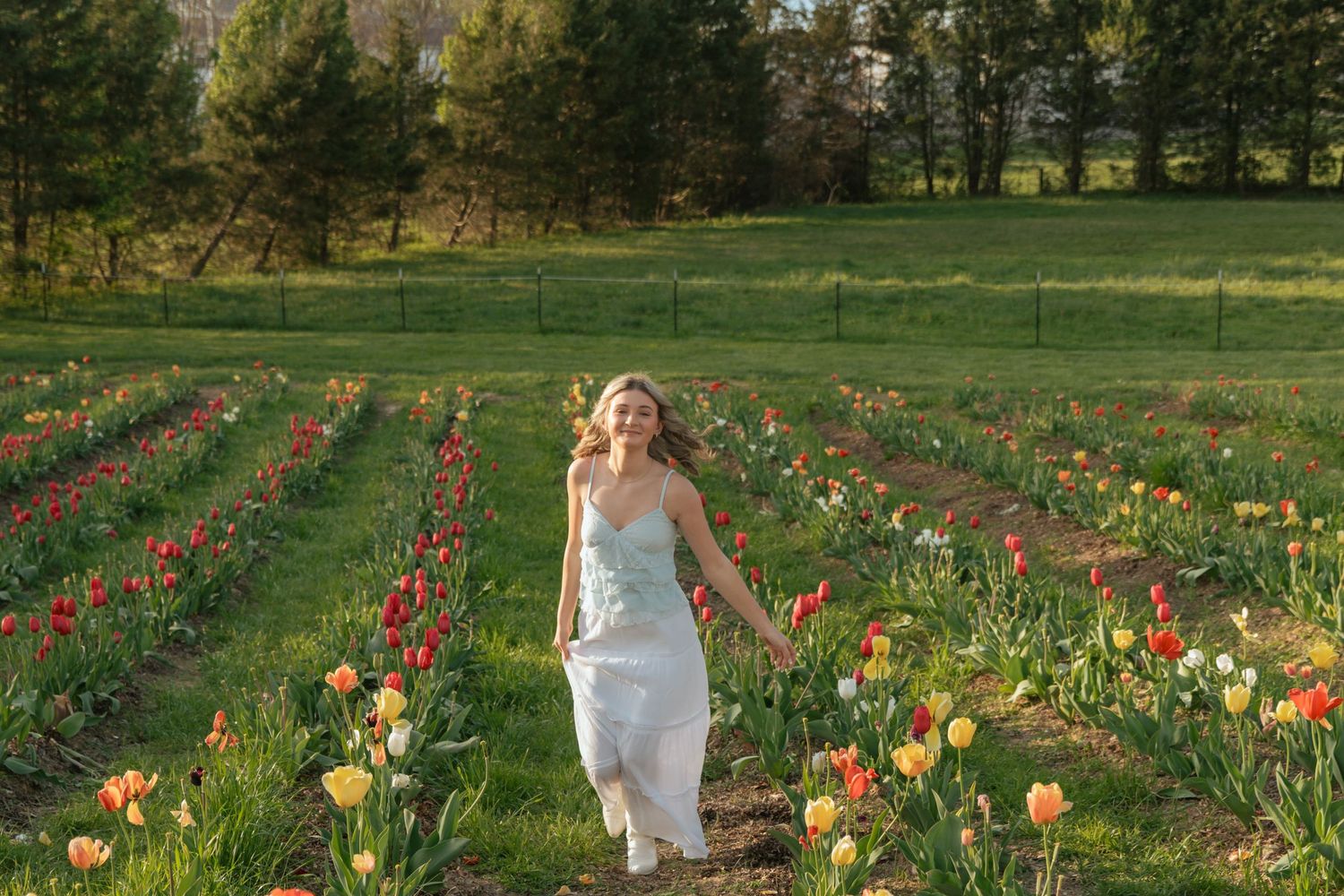 Woman in white dress walking through colorful tulip field on sunny spring day.