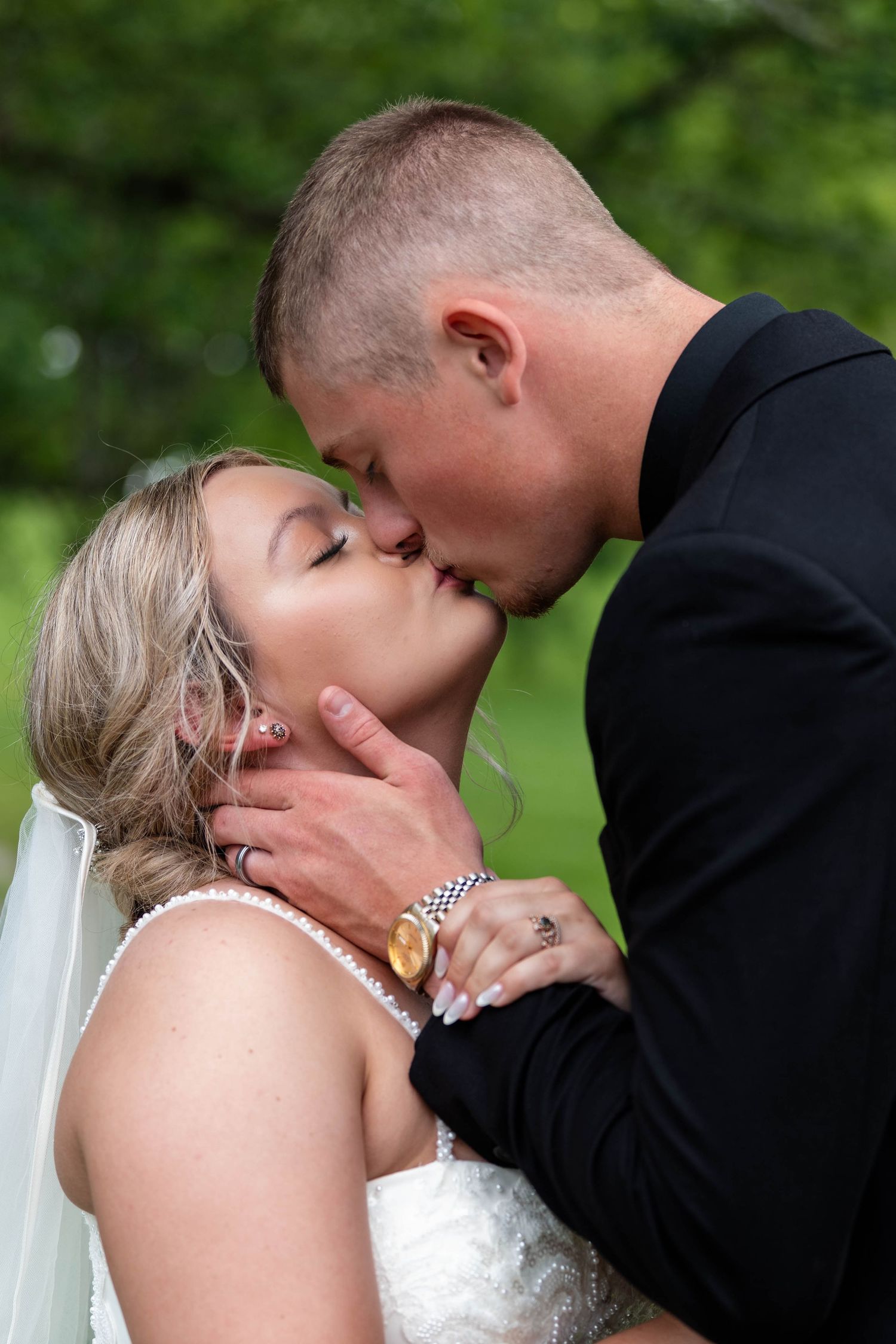 Bride and groom share a tender kiss outdoors, with the groom gently cradling her face on their wedding day.