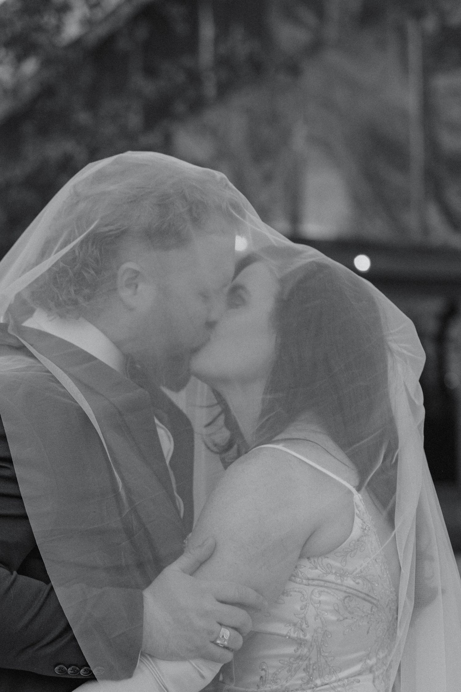 Black and white photo of bride and groom kissing under a sheer wedding veil.