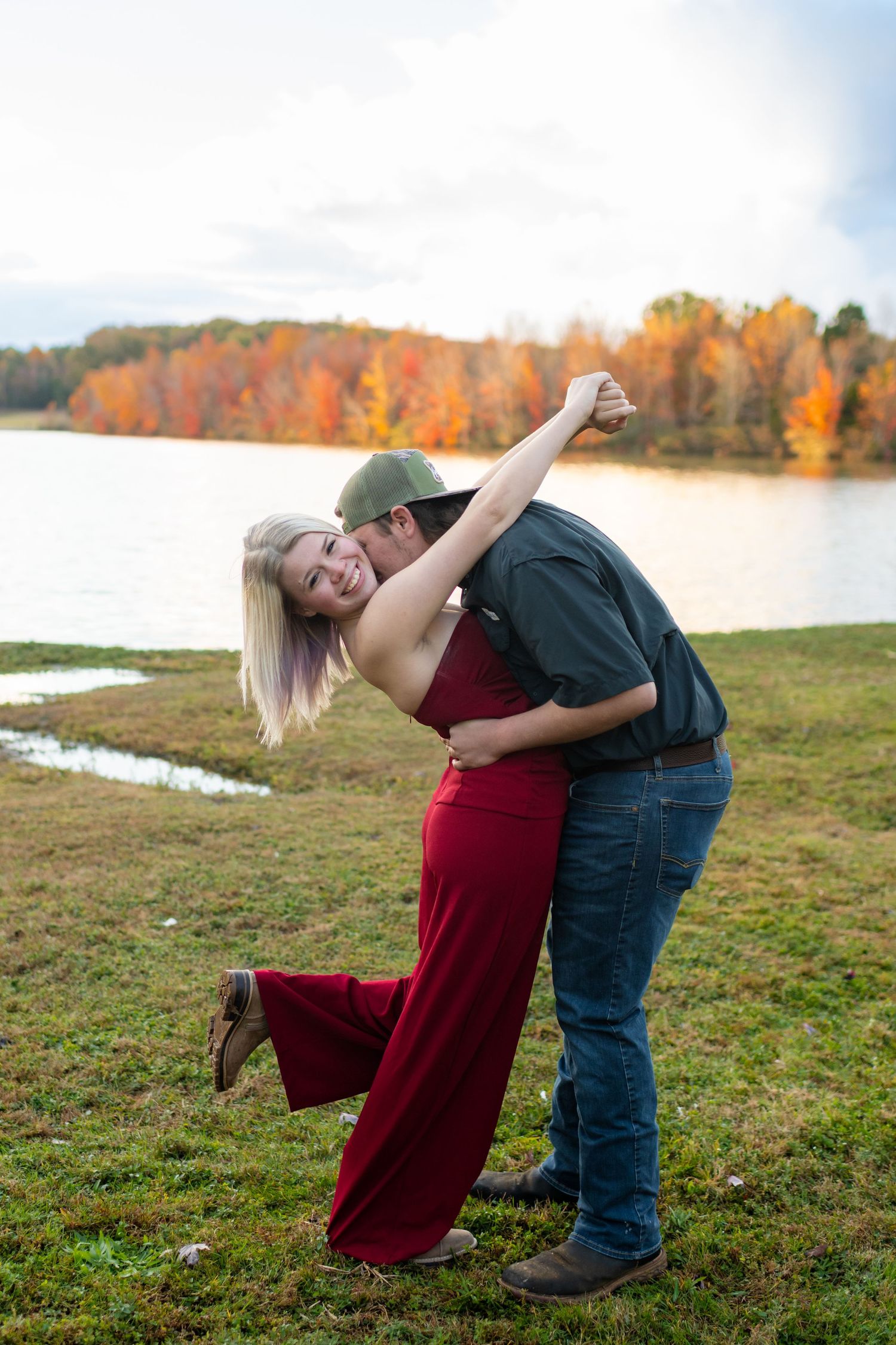 Joyful couple dancing and laughing by lakeside surrounded by colorful fall foliage.