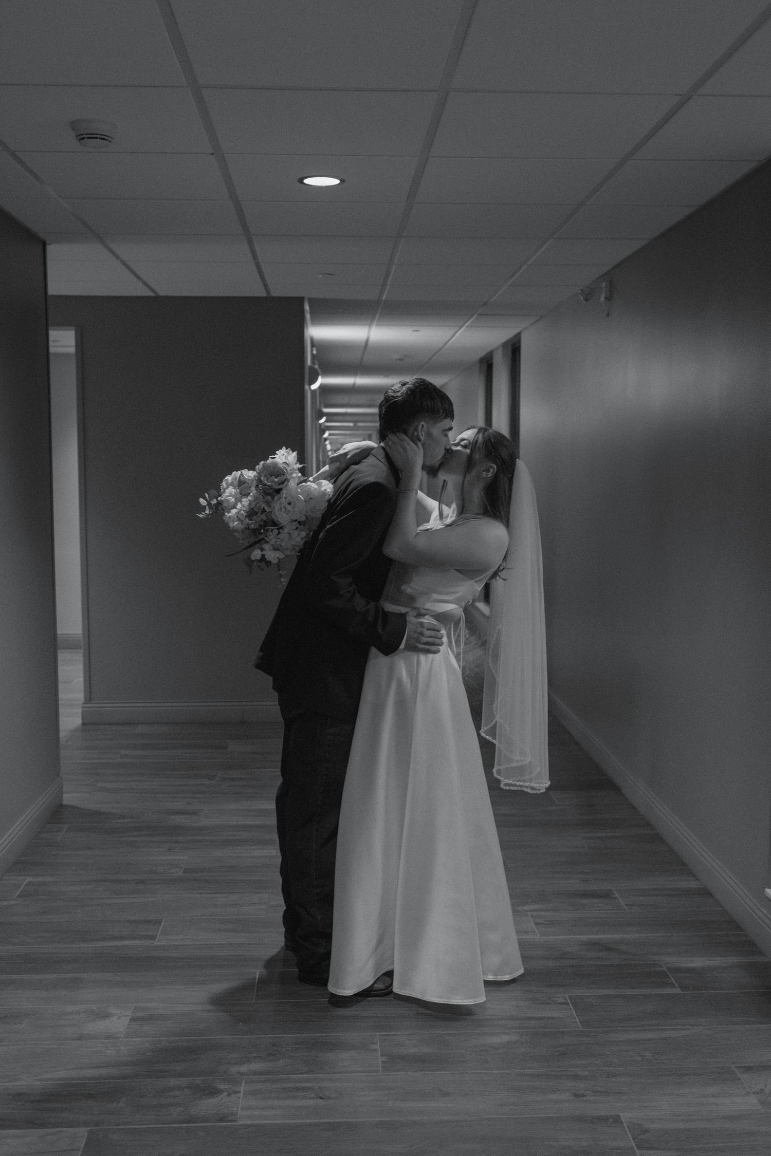 Black and white photo of bride and groom sharing a kiss in a hallway.