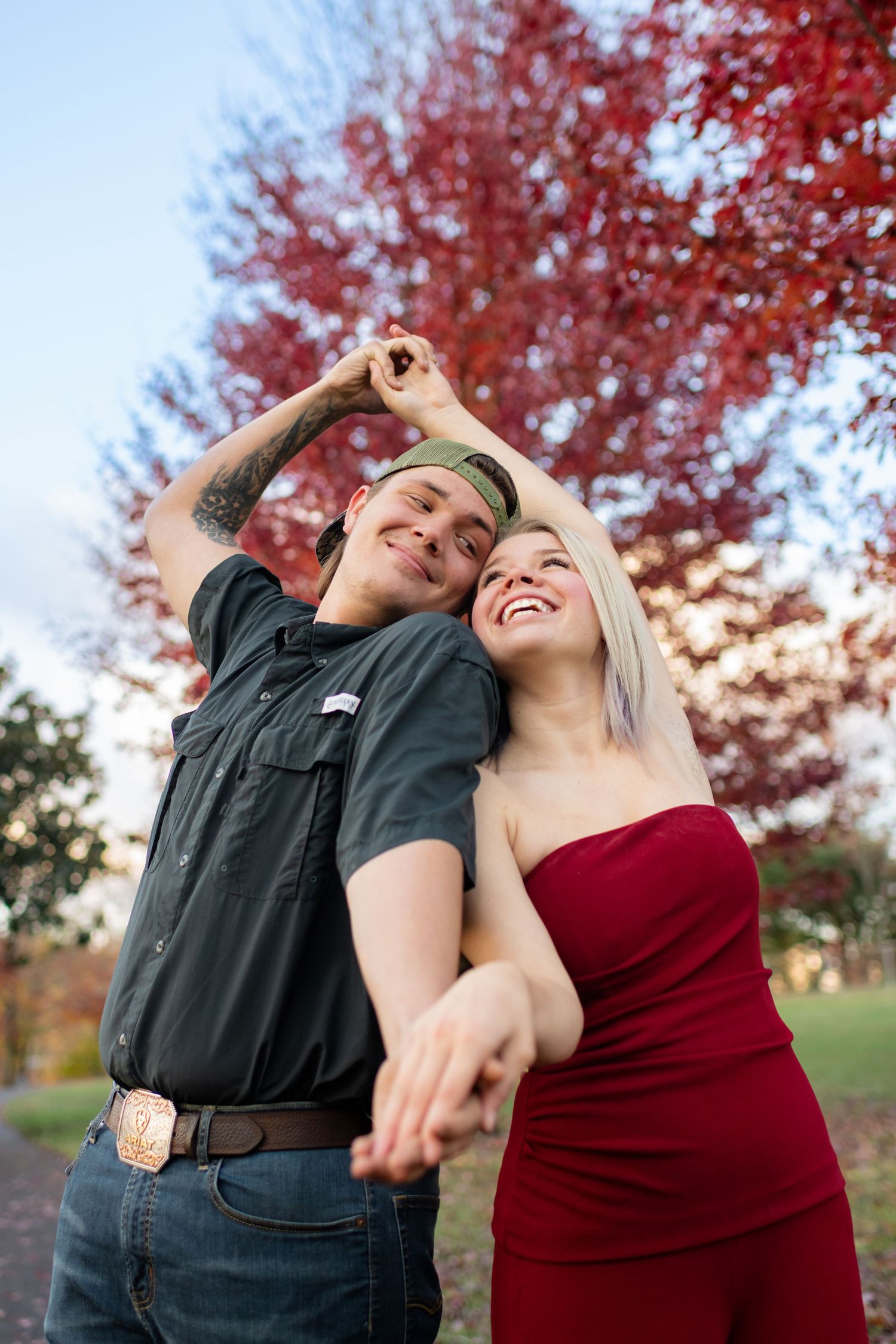 Joyful couple dancing and laughing together beneath a stunning red autumn tree in a park setting.