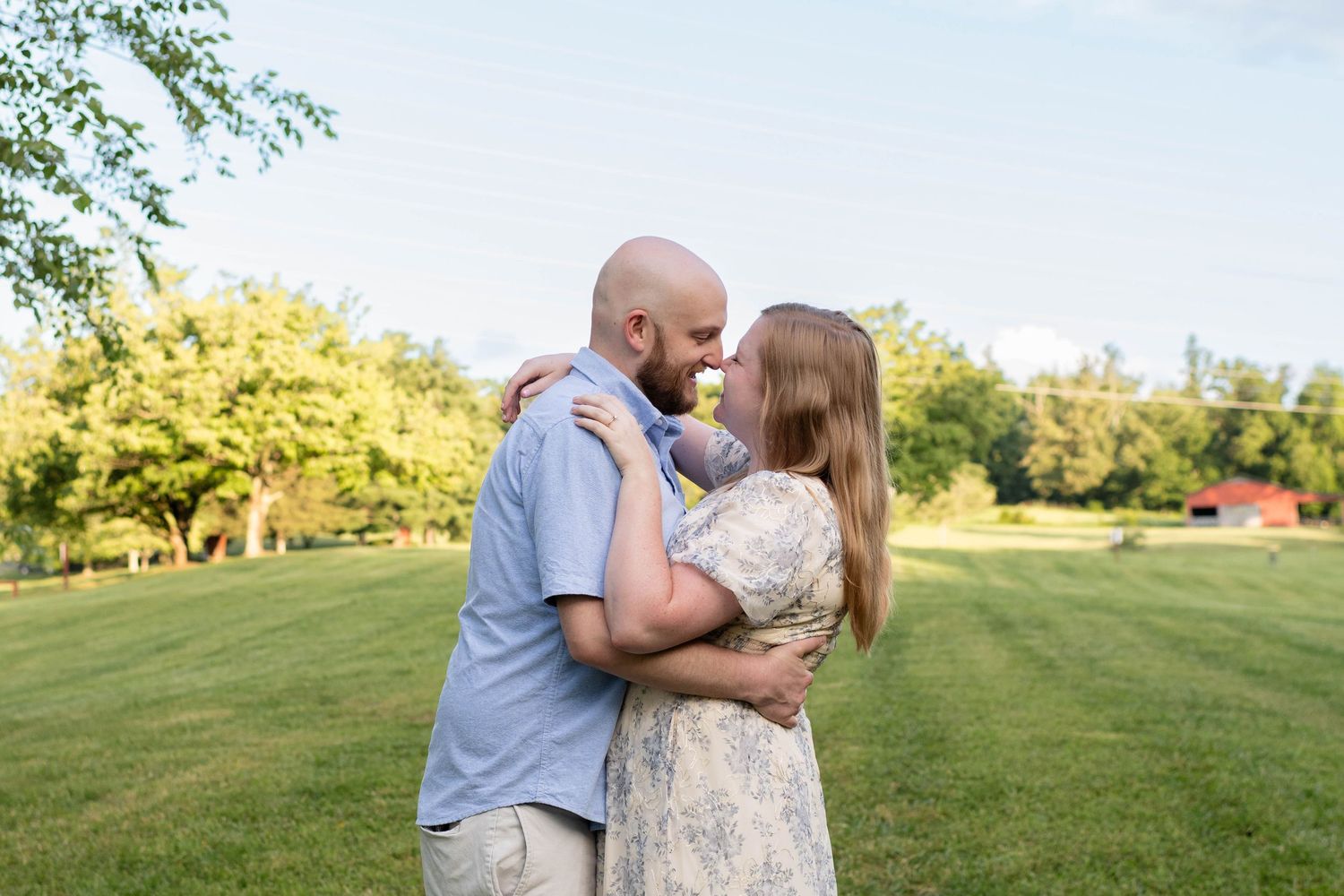 Happy engaged couple embracing and smiling at each other in a lush green garden on sunny day.