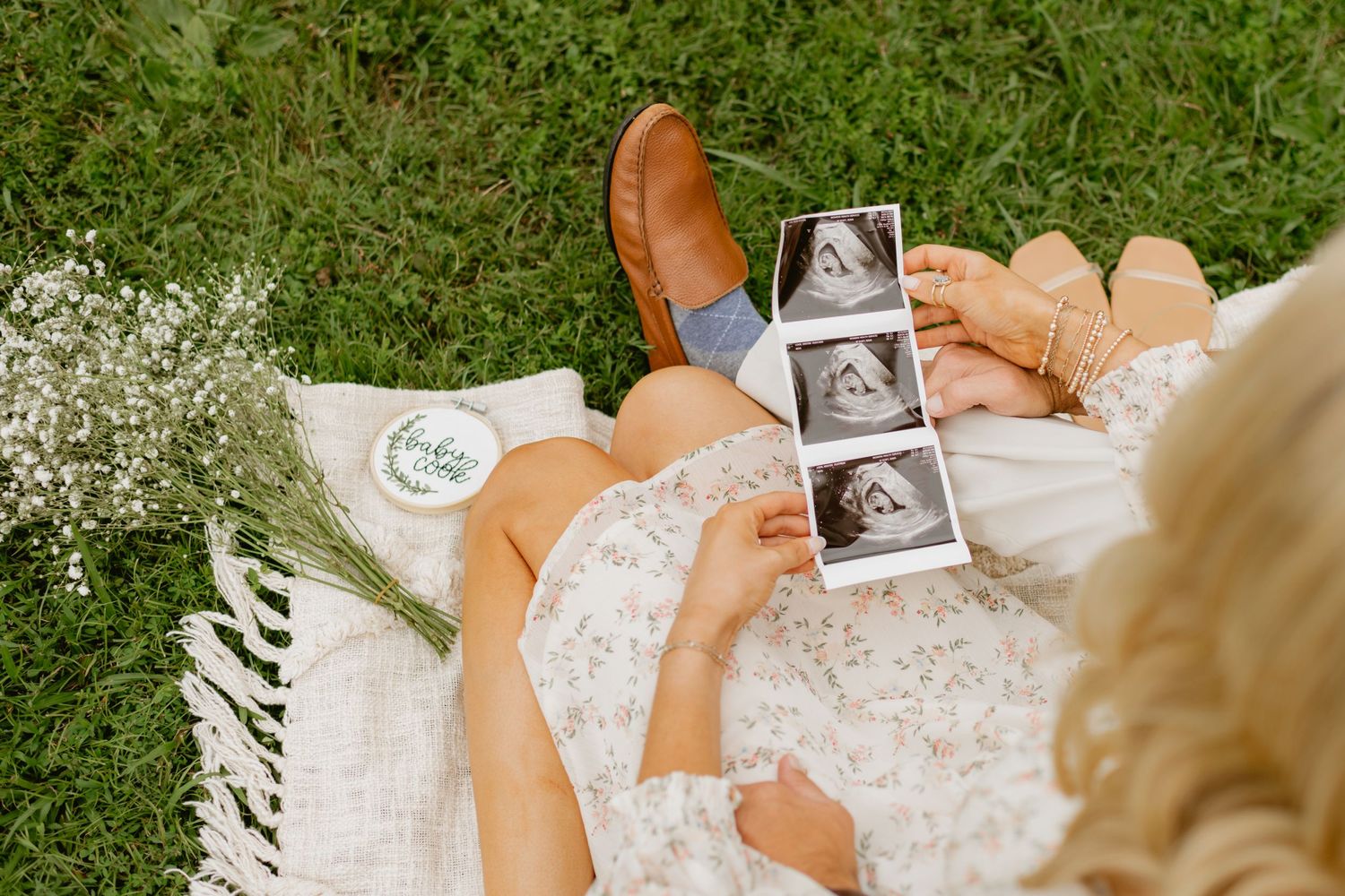 Overhead view of couple on blanket holding ultrasound images with baby name sign on grass.