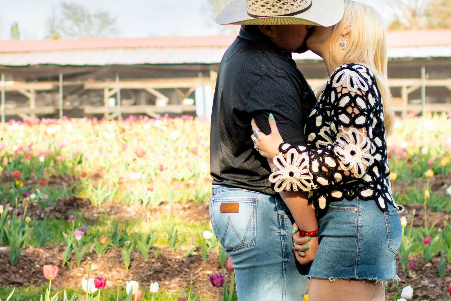 Couple sharing a kiss surrounded by vibrant tulip flowers in a sunny garden field.