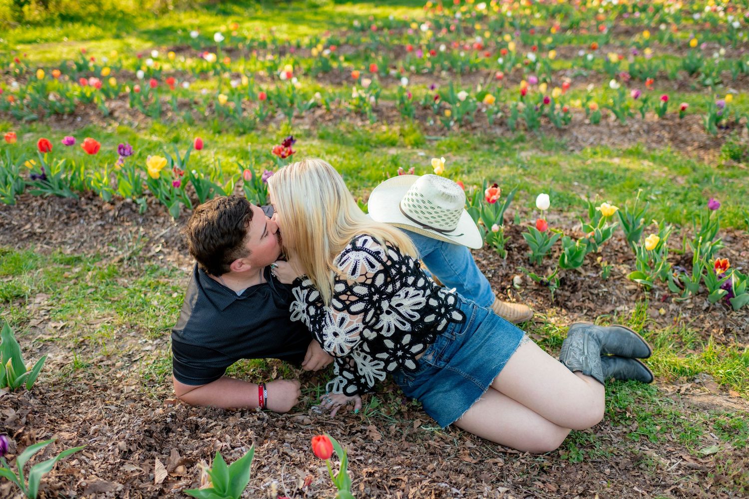 Couple sharing a romantic kiss while lying in a colorful tulip garden on a sunny day.