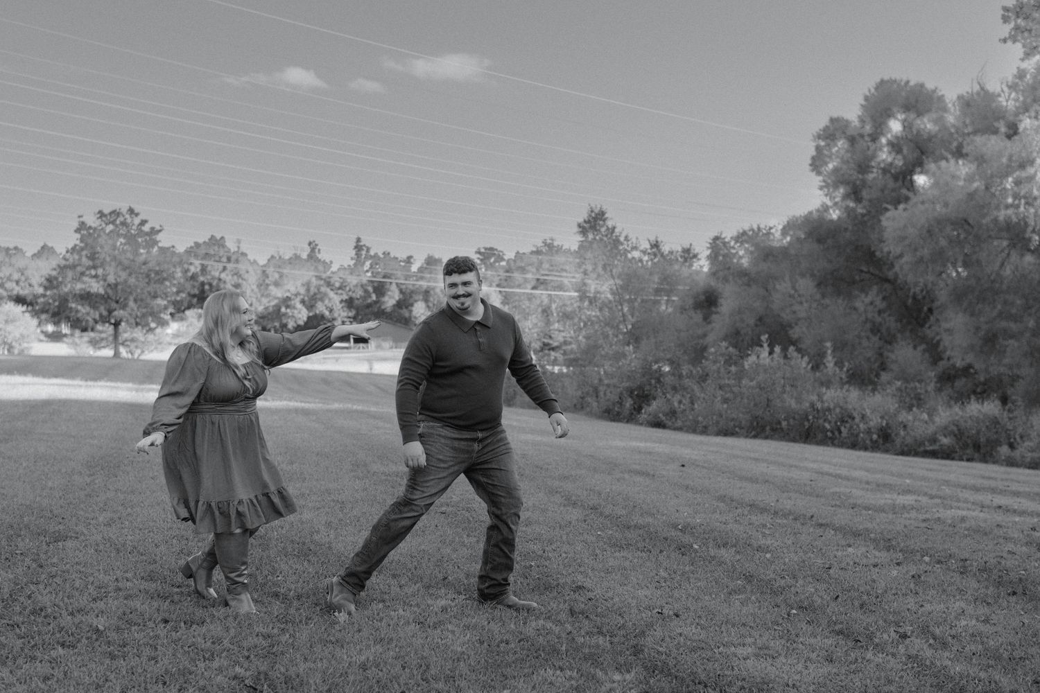 Black and white photo of a playful couple dancing together on a grassy outdoor lawn.