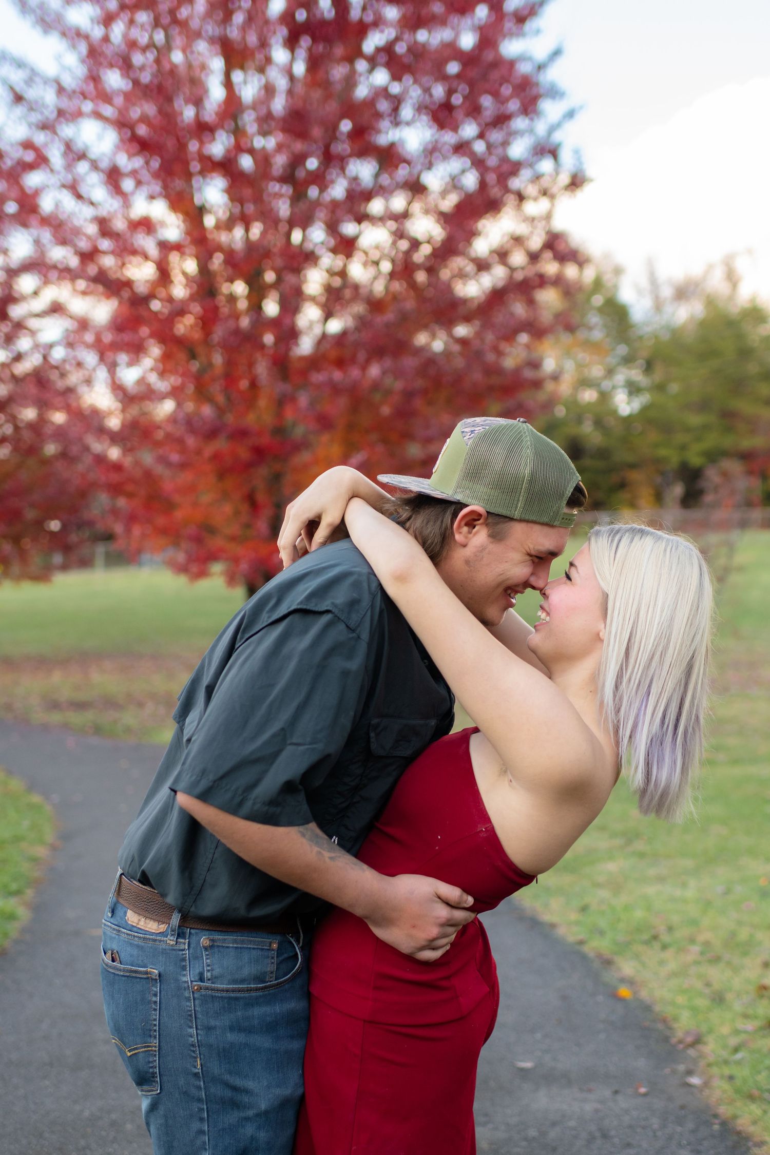 Happy couple embracing and laughing together in front of a vibrant red autumn tree in a park.