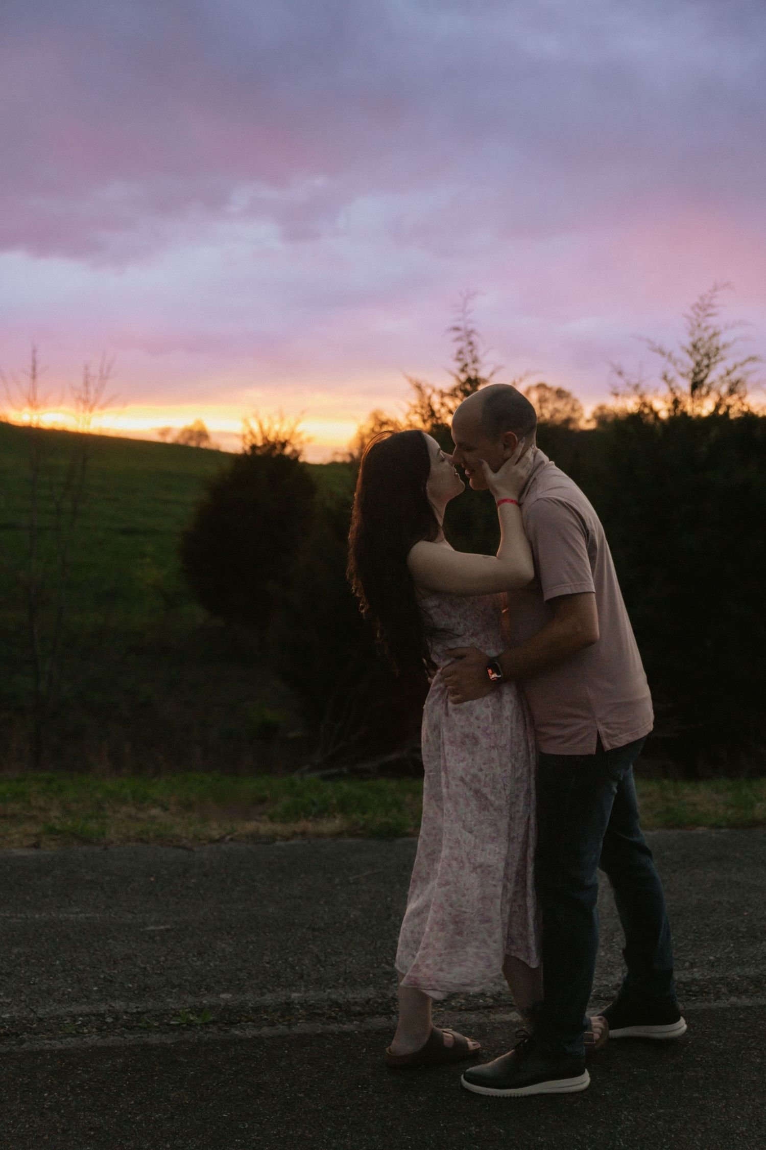 Couple sharing a kiss at golden hour sunset with colorful purple and orange sky behind them.