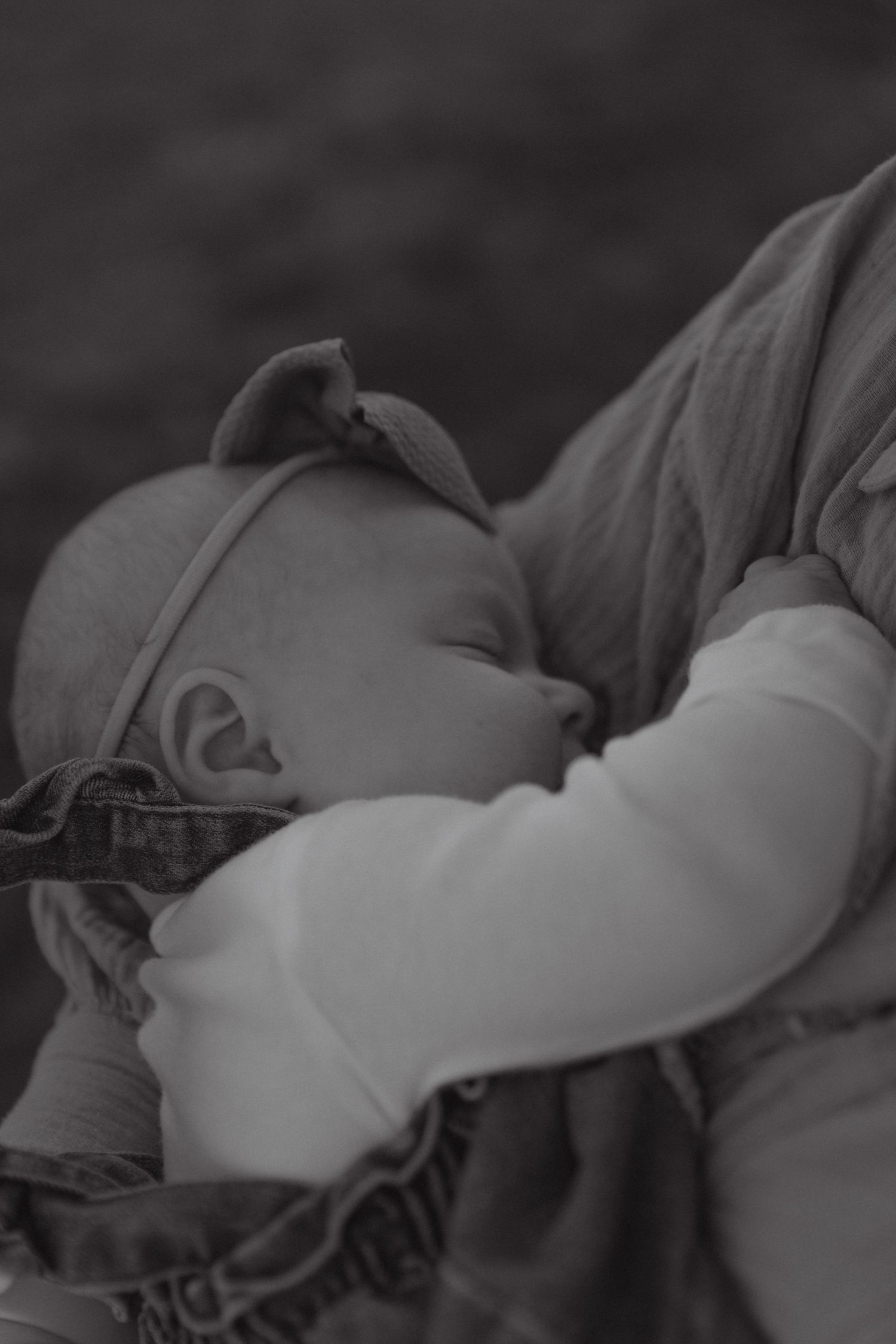 Black and white portrait of peaceful sleeping newborn baby with bow headband in mothers arms.