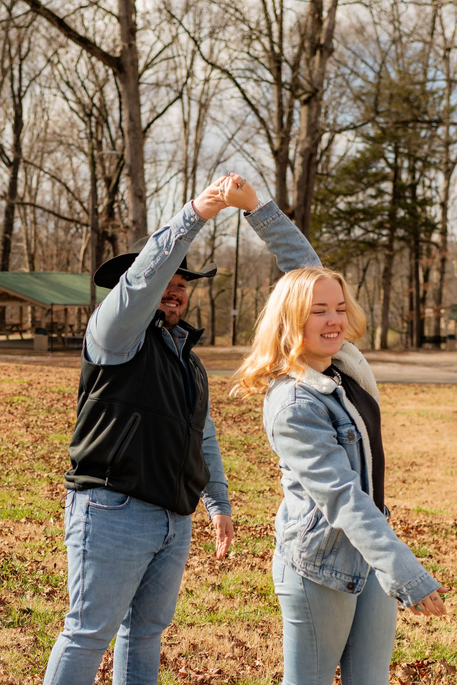 Couple dancing outdoors in a park, man in cowboy hat spinning blonde woman in denim jacket on grass.