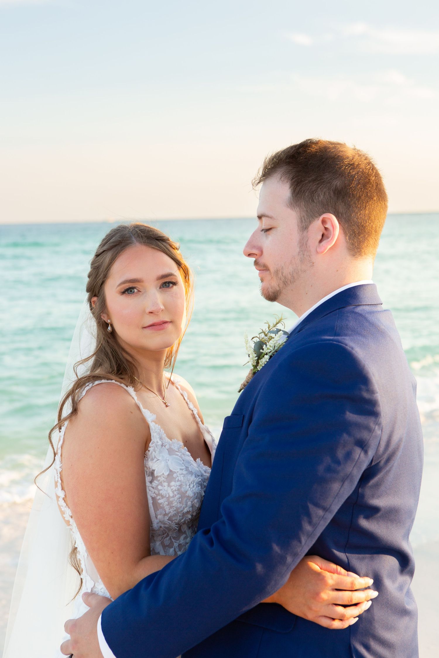 Bride and groom embrace on a beach with turquoise ocean backdrop during their seaside wedding ceremony.