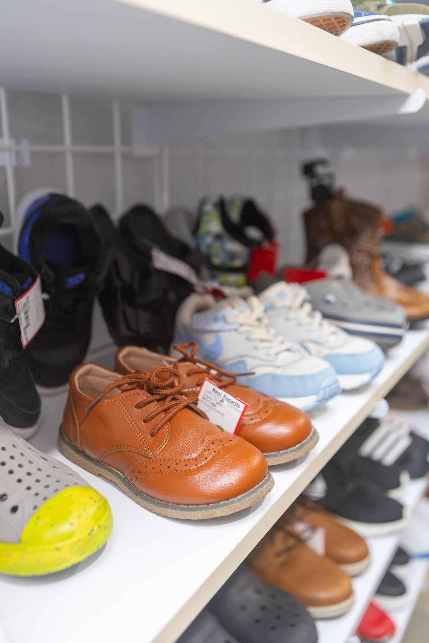 Children's shoes displayed on white shelves, featuring brown leather lace-up shoes in the foreground.