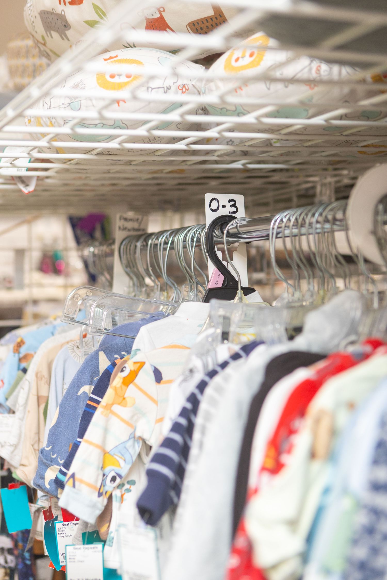 Baby clothes sized 0-3 months hanging on metal rack in a children's resale clothing store.