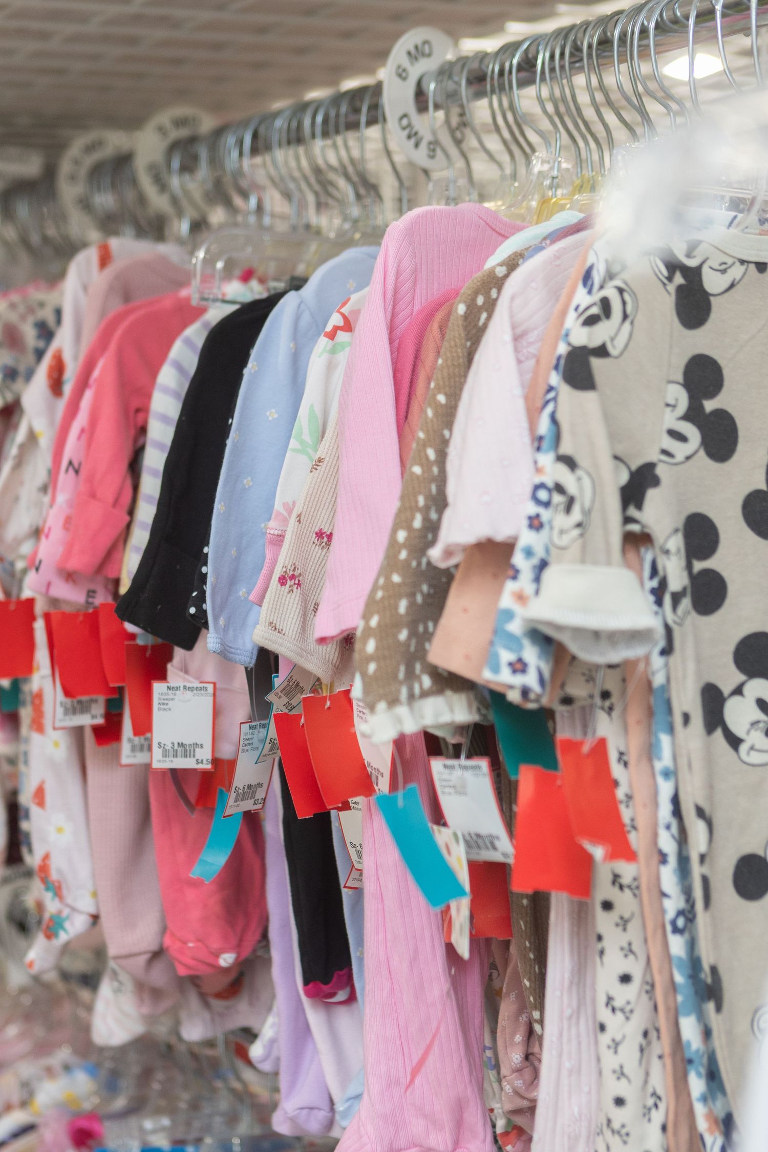 Colorful children's clothing hanging on a retail rack with red and teal price tags in a clothing store.