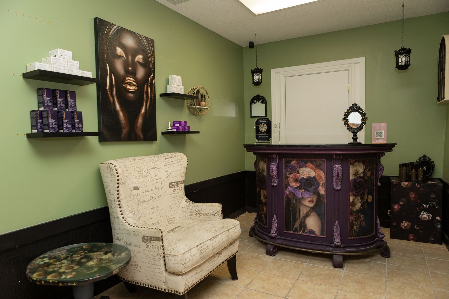 Elegant spa reception area with green walls, ornate purple desk, gold portrait art, and a cream wingback chair.