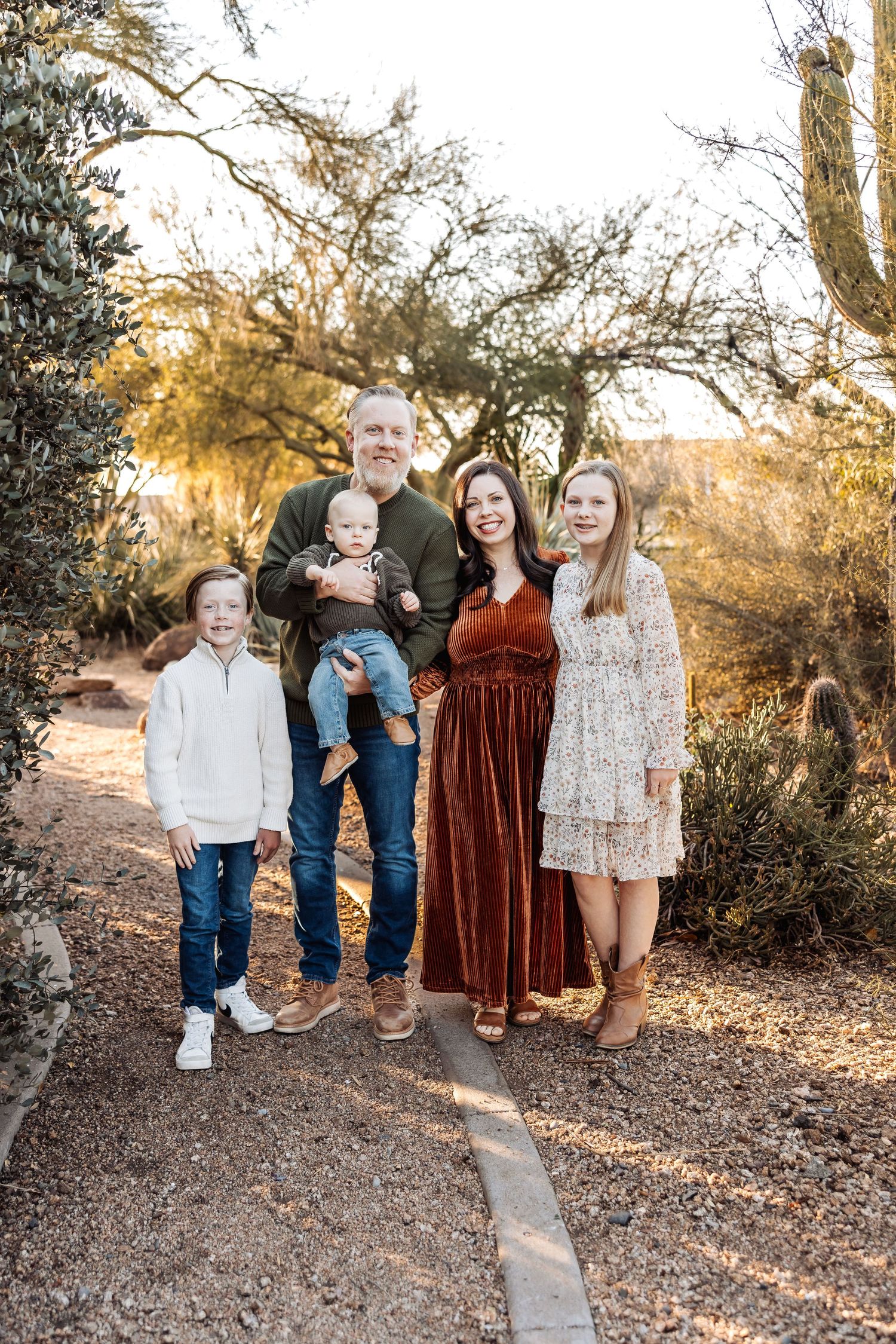 A family poses together in a desert landscape during golden hour with cacti and trees in the background.
