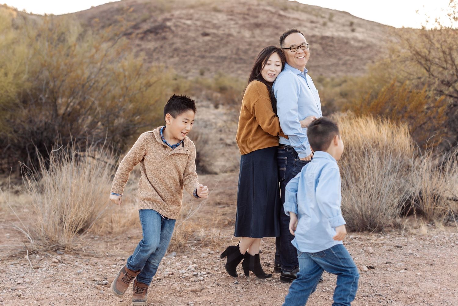 A family wearing coordinated casual outfits enjoys time together in a desert setting with brown hills and brush in the background.