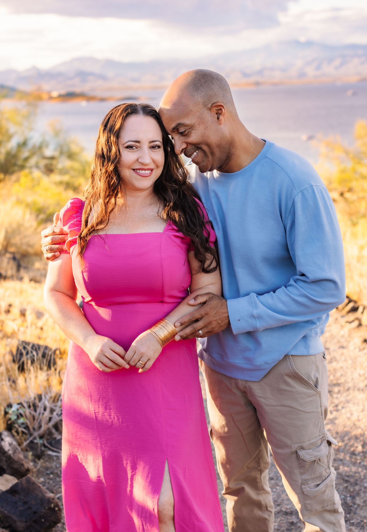 A couple shares tender moments together in a desert landscape during golden hour in matching pink and blue outfits.