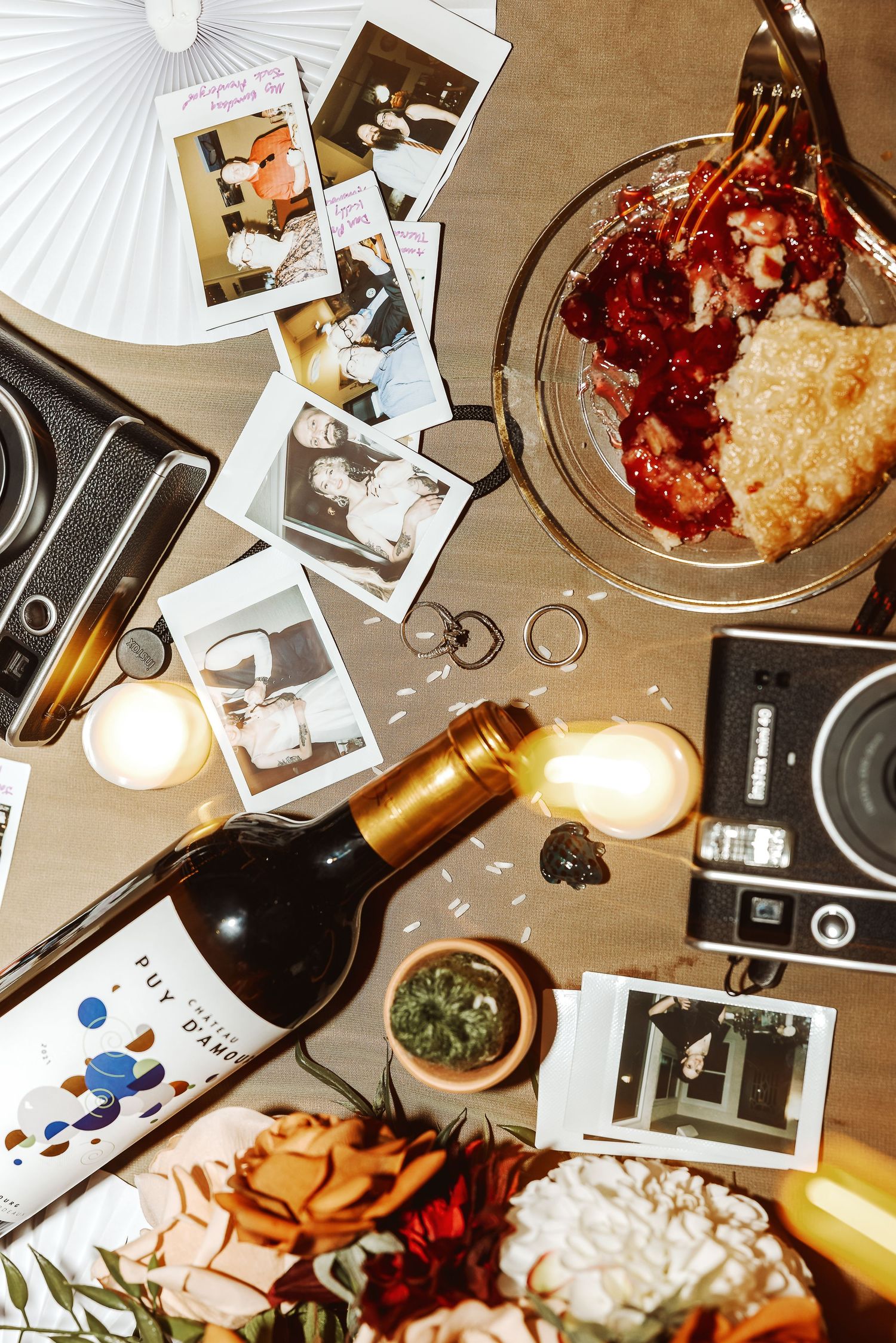 Artistic wedding detail photography with scattered polaroid photos, wine glasses, and decorative elements on a table.