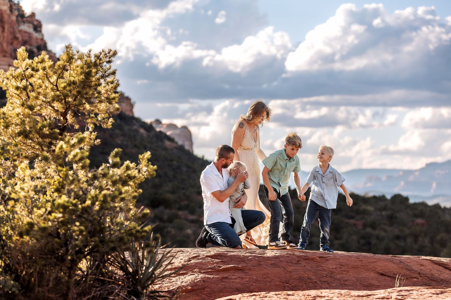 Family enjoying a sunset moment together on red rocks with dramatic cloudy sky in the background.
