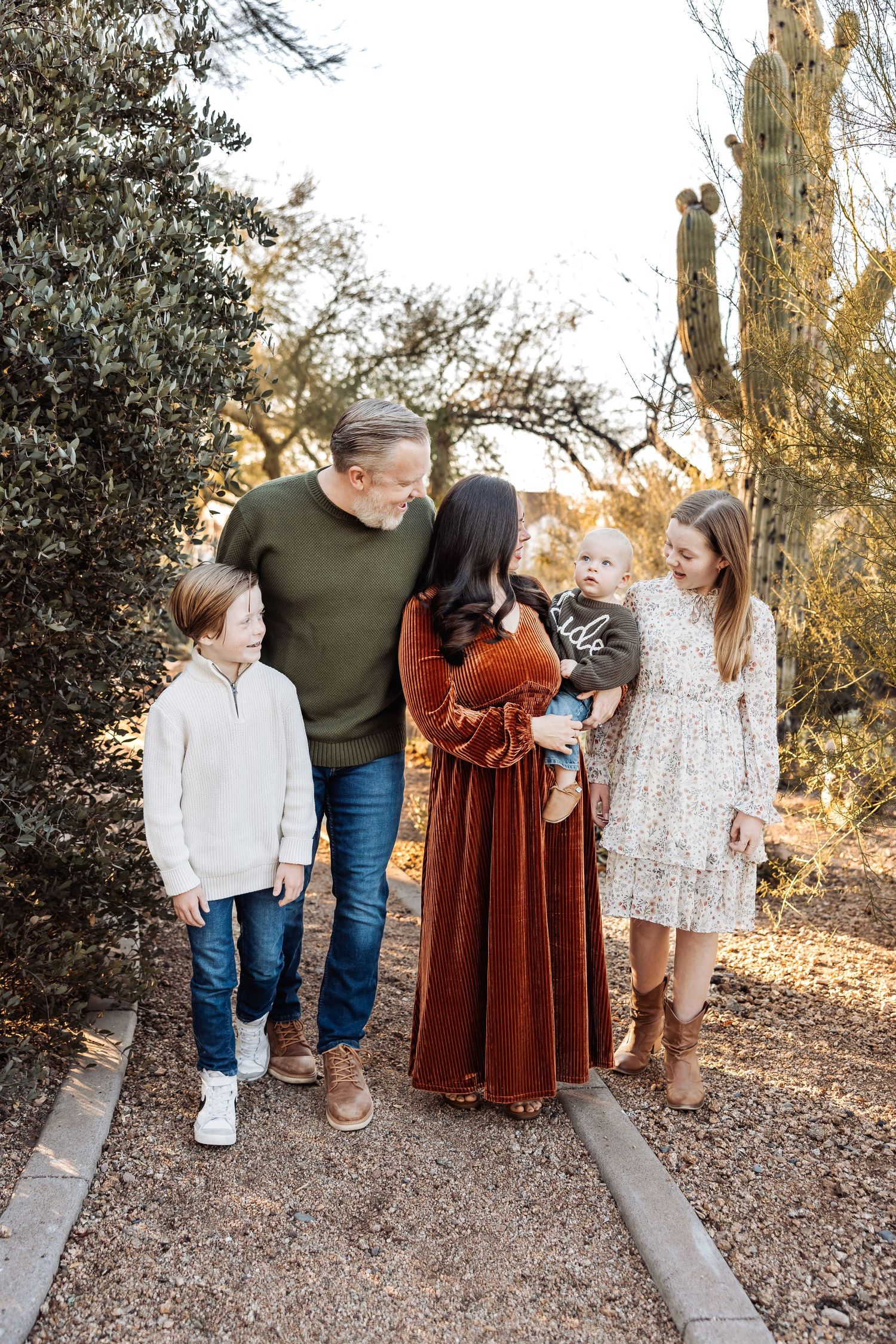 Family of four smiling together on outdoor path during golden hour with cacti and desert plants in background.