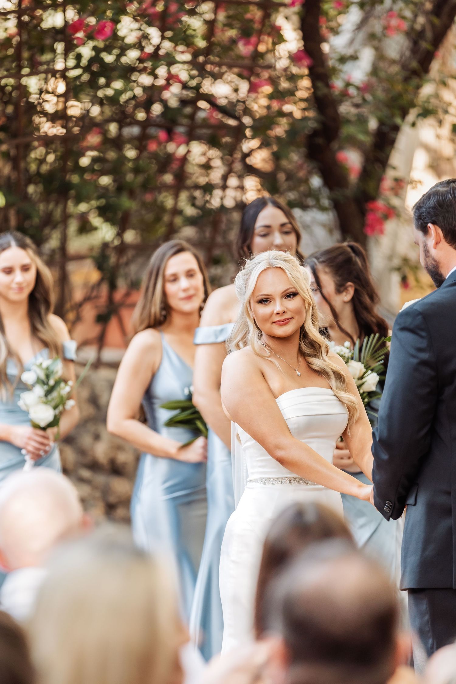 Wedding party poses outdoors with bridesmaids in light blue dresses and bride in white gown.