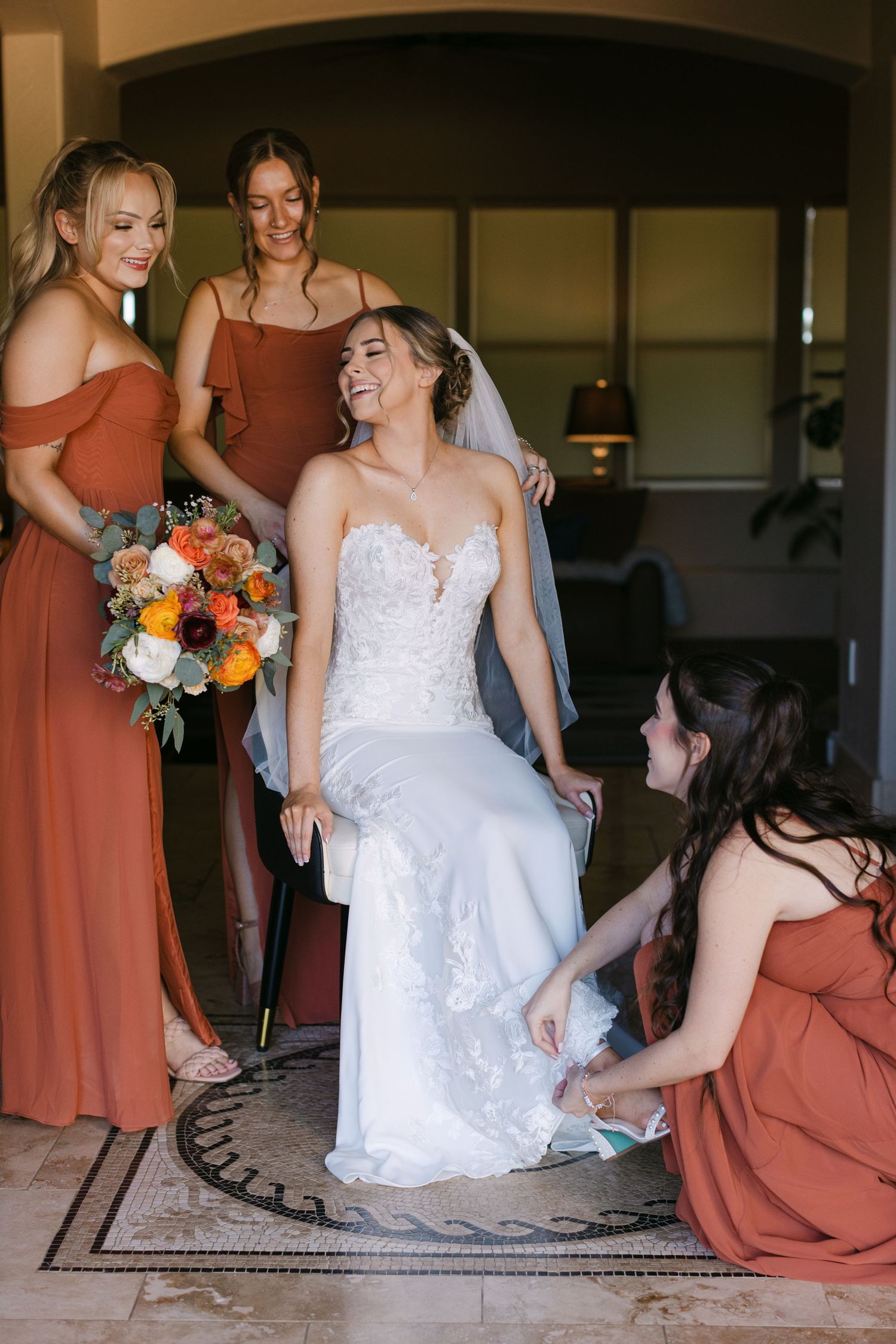 Bridesmaids in terracotta dresses help adjust the bride's gown while colorful bouquets add bright accents.