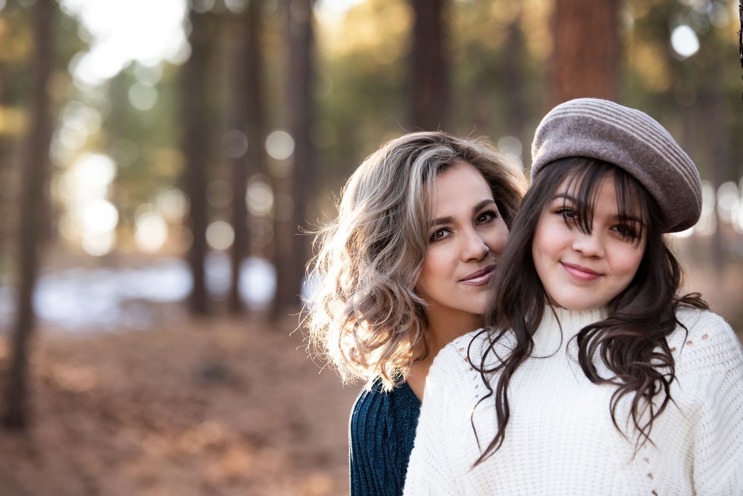 Two women in winter clothes smiling together outdoors with trees in background.